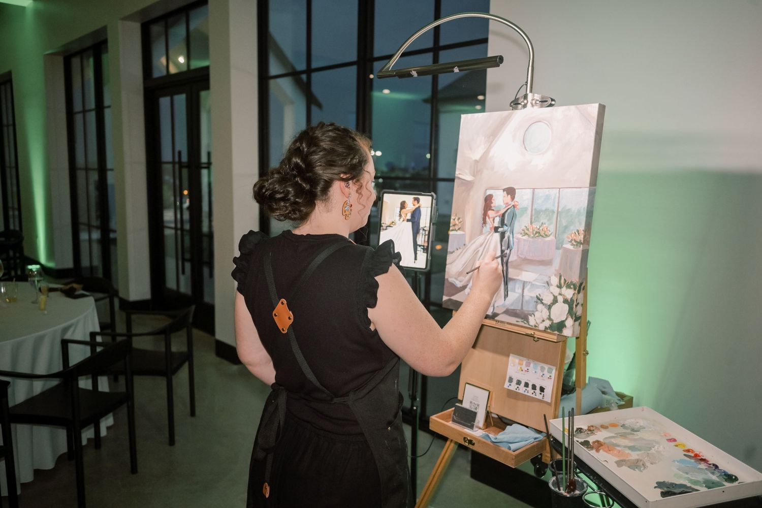 Artist paints a live wedding portrait on an easel at an elegant evening reception.