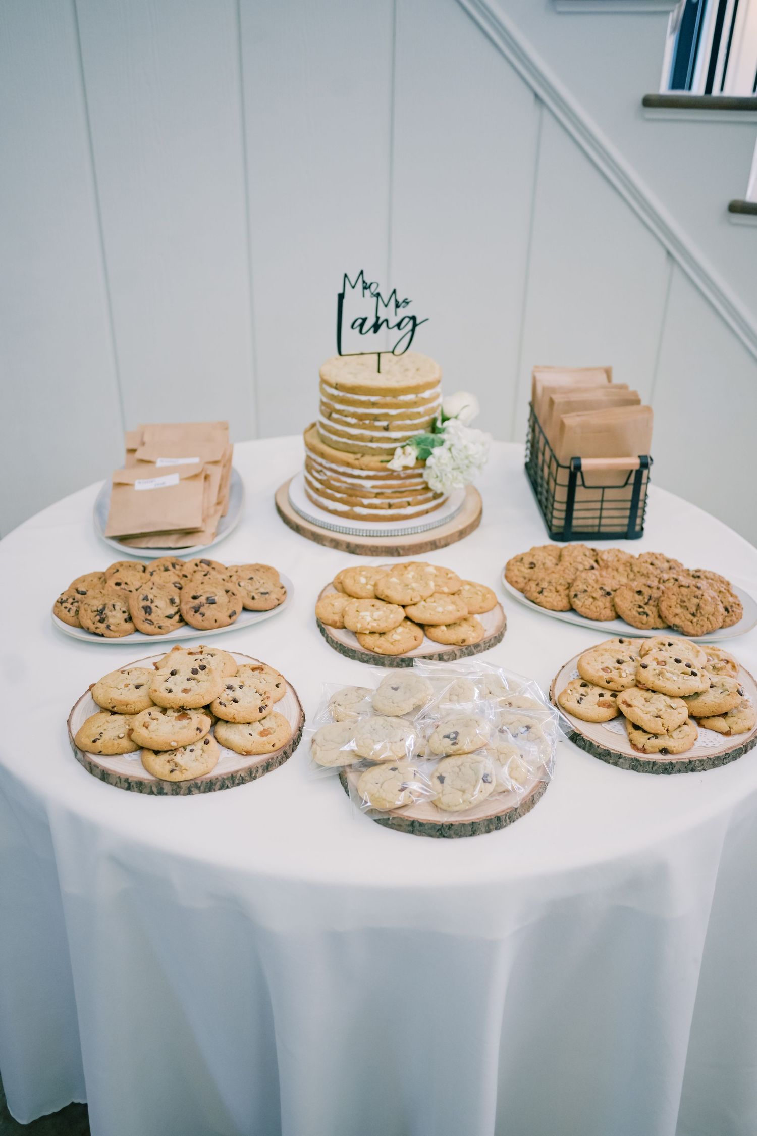 Wedding dessert table with naked cake, Mr. and Mrs. topper, and assorted cookies on wood slices.