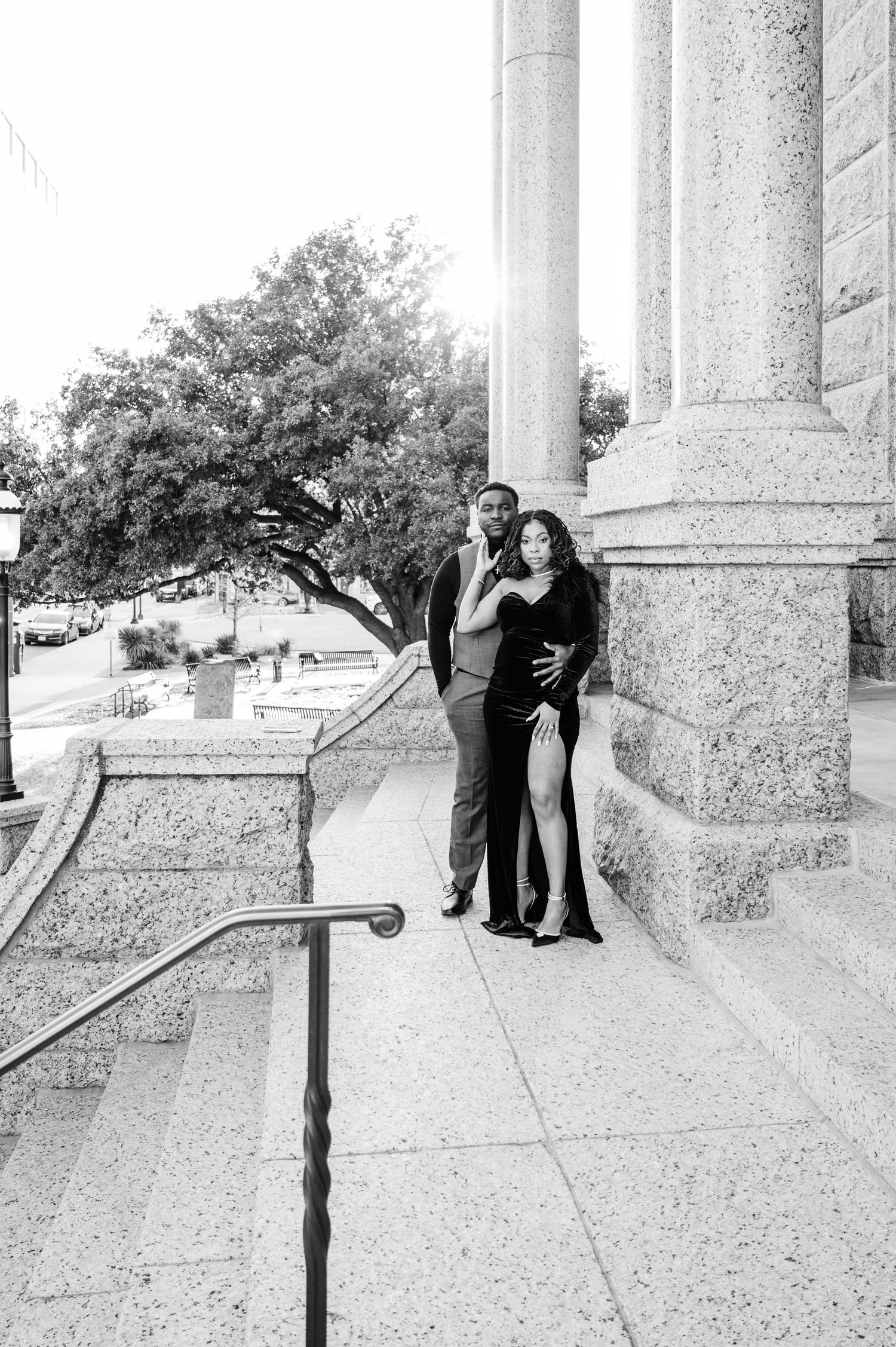Black and white photo of an elegant couple posing on grand stone steps near large columns.