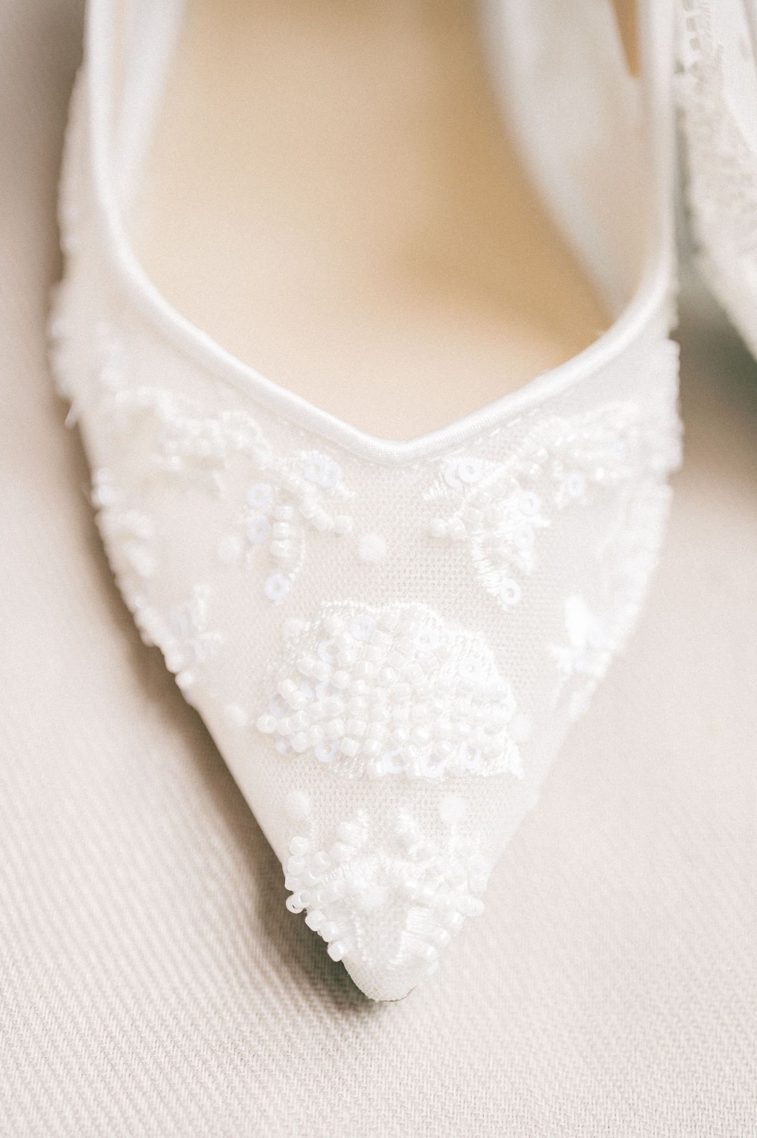 Close-up of delicate white beaded bridal shoes with lace detail.