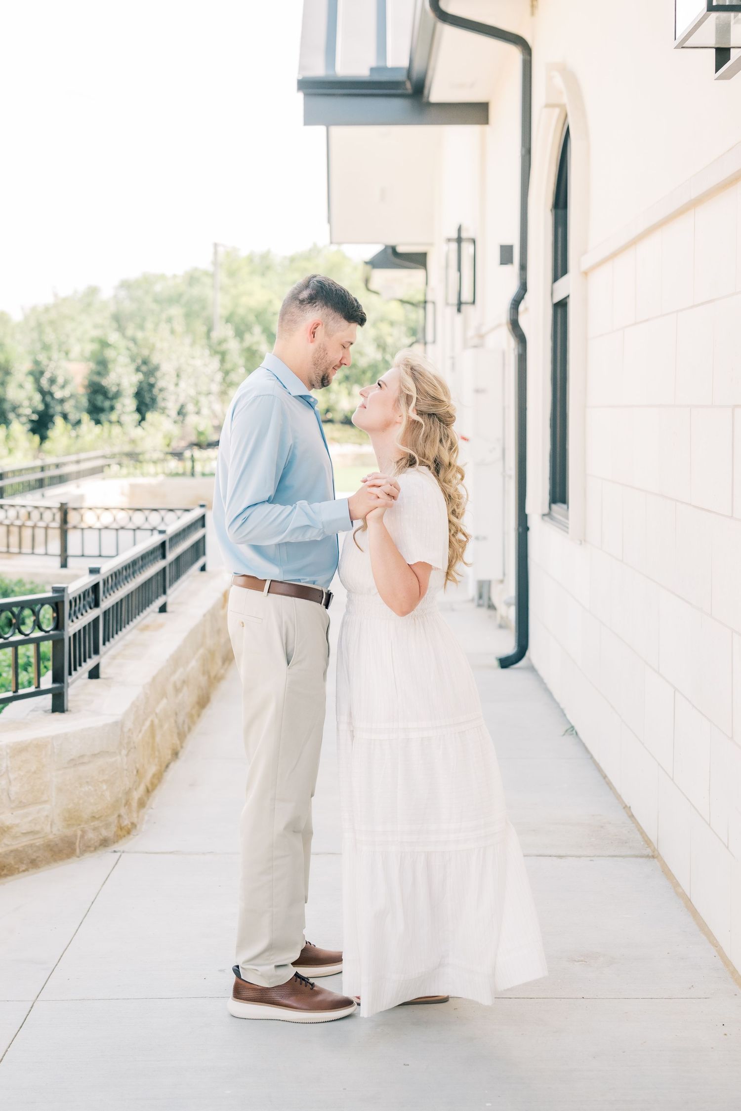 Couple sharing a romantic moment on a sunlit outdoor walkway, woman in white dress and man in blue shirt.