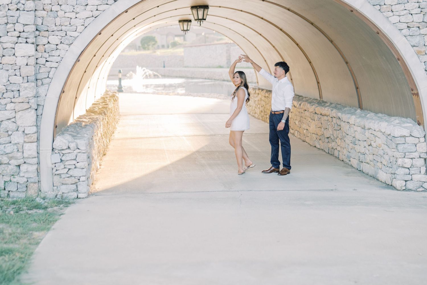 A couple shares a playful dance moment under a curved stone archway during their engagement session.