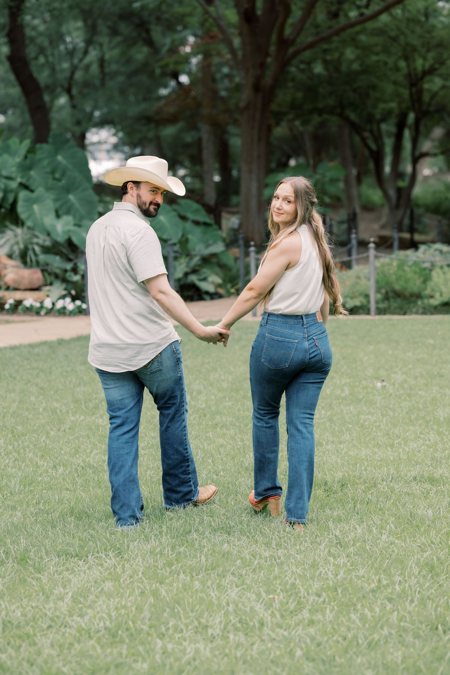 Couple holding hands on a green lawn, both wearing jeans and cowboy boots.