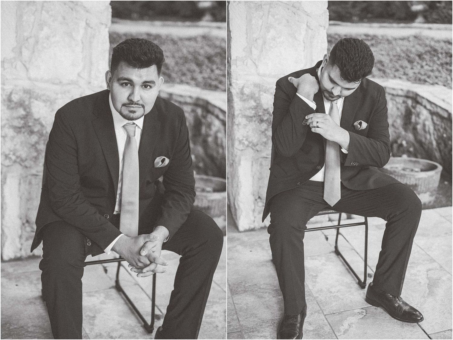 A groom in a black suit sits thoughtfully on stone steps during a wedding photoshoot.