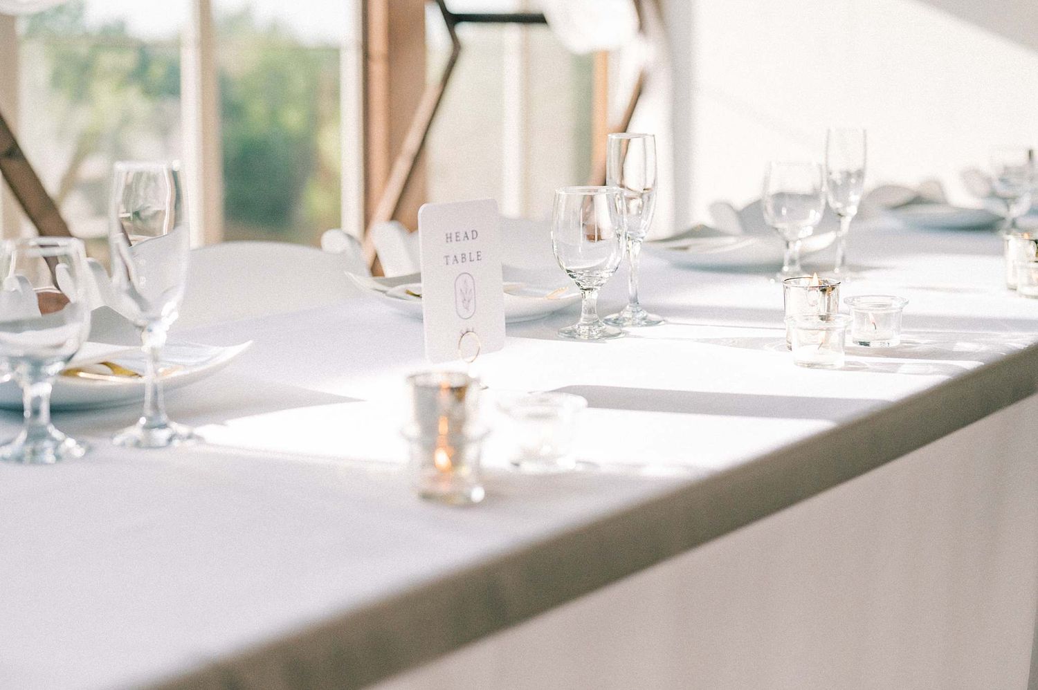 Bright sunlit banquet table setup with white tablecloths and formal place settings.