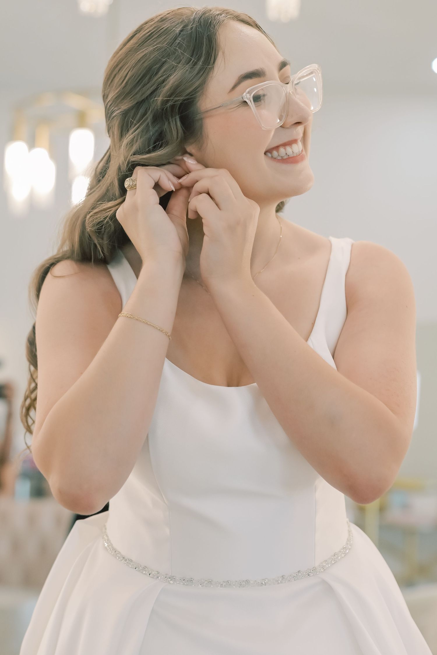 Smiling bride in white gown adjusting earrings while getting ready on her wedding day.