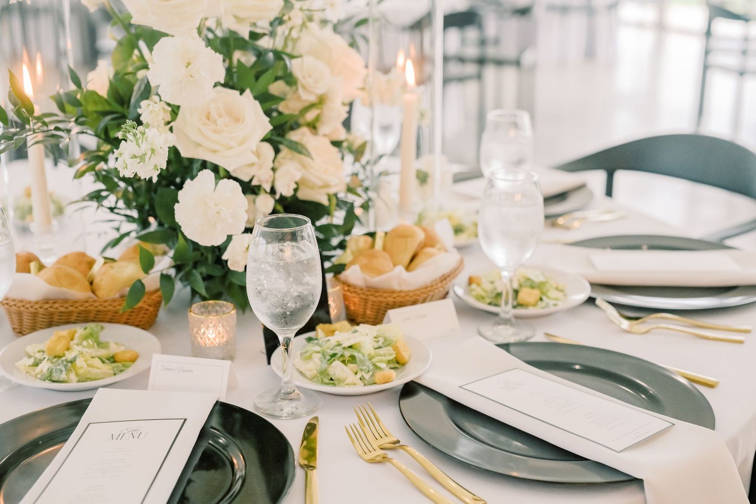 Elegant wedding reception tablescape with white floral centerpiece, gold cutlery, and green chargers.
