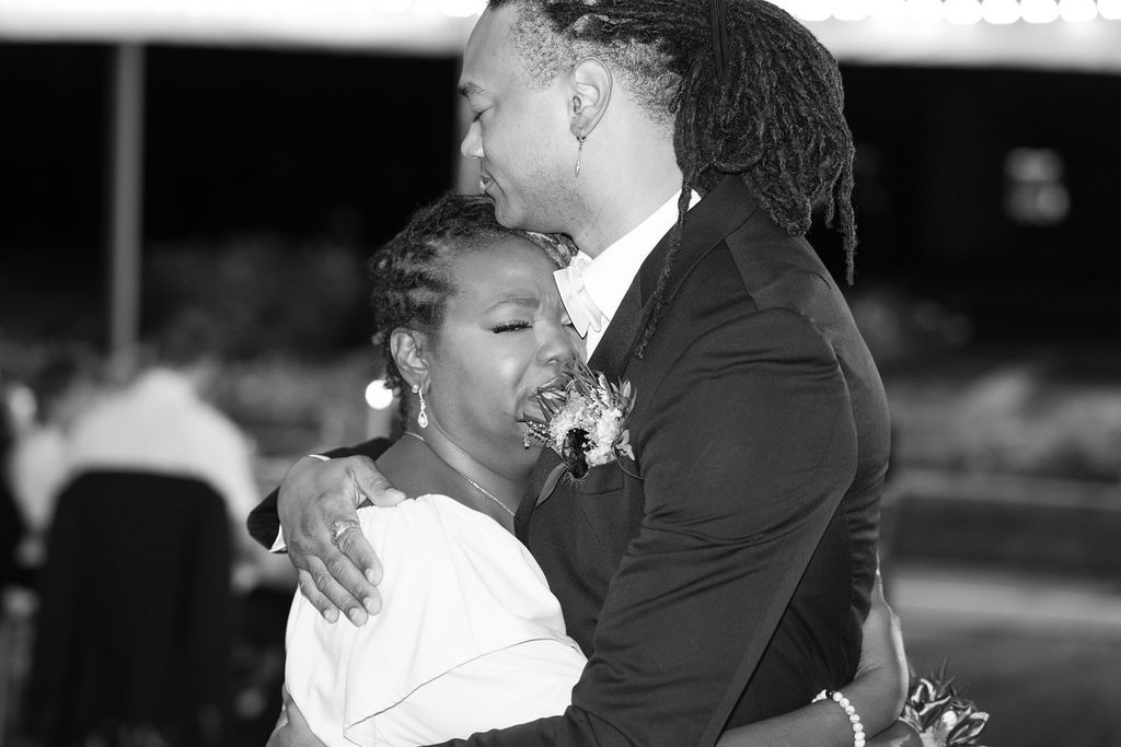 Black and white photo of a couple sharing an emotional dance embrace at a wedding reception.
