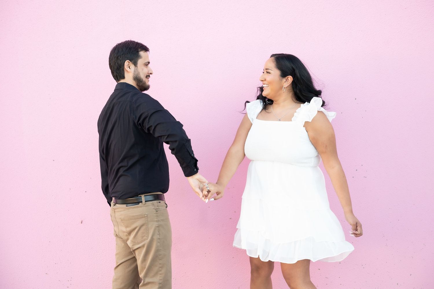 A couple in wedding attire dances and poses playfully against a pink background in a photo series.
