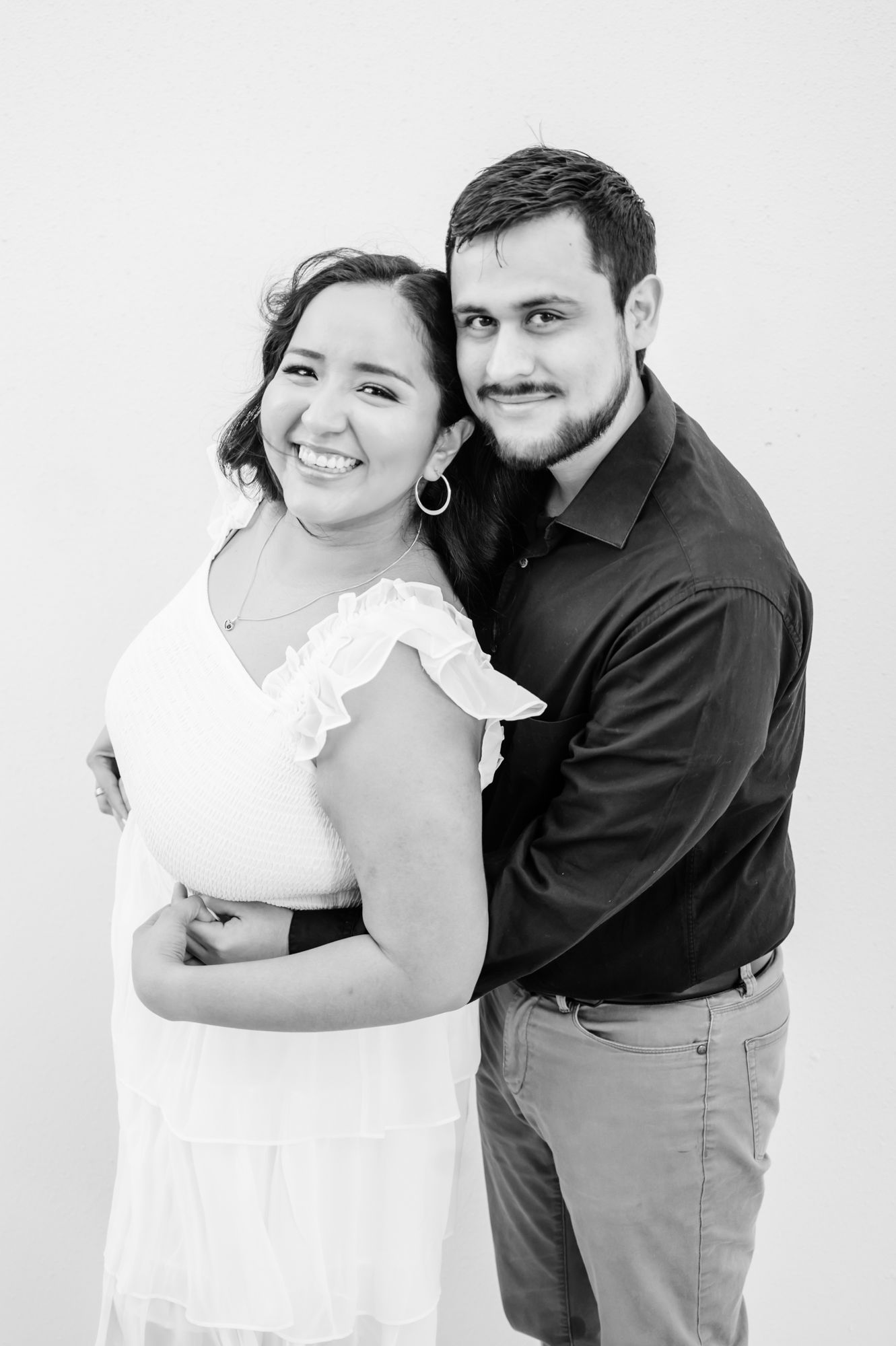 A romantic couple in white and black outfits embracing in a series of sweet poses against a light background.