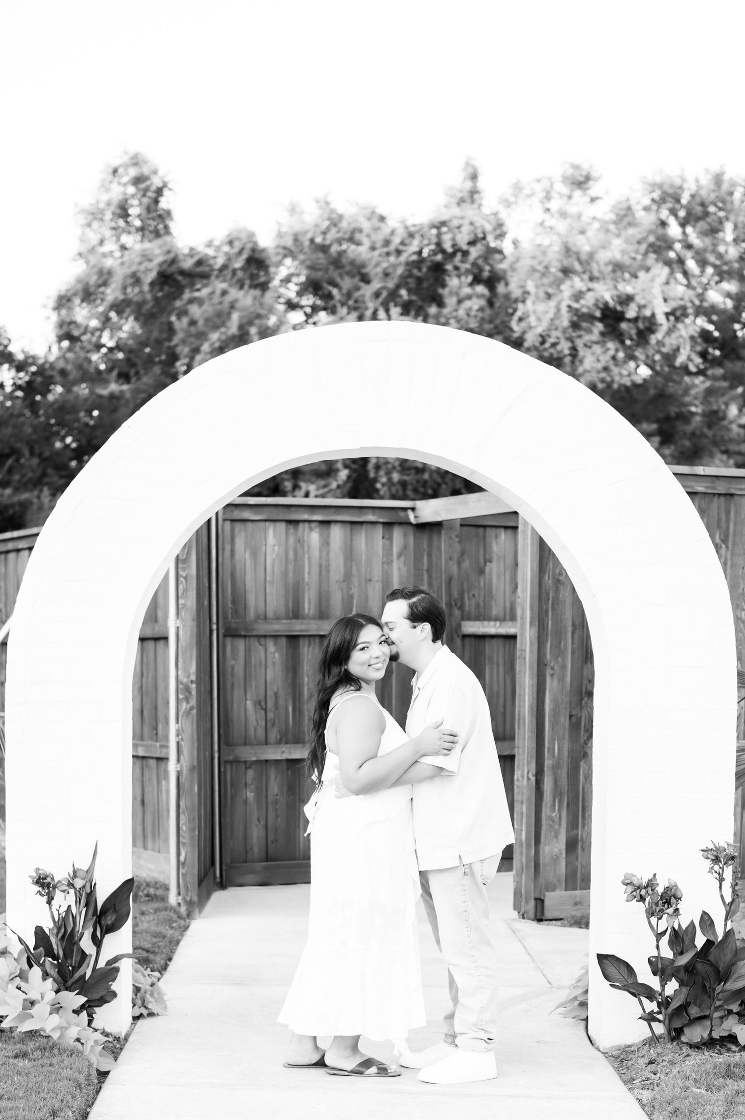 A series of black and white engagement photos showing a couple in a backyard garden setting.
