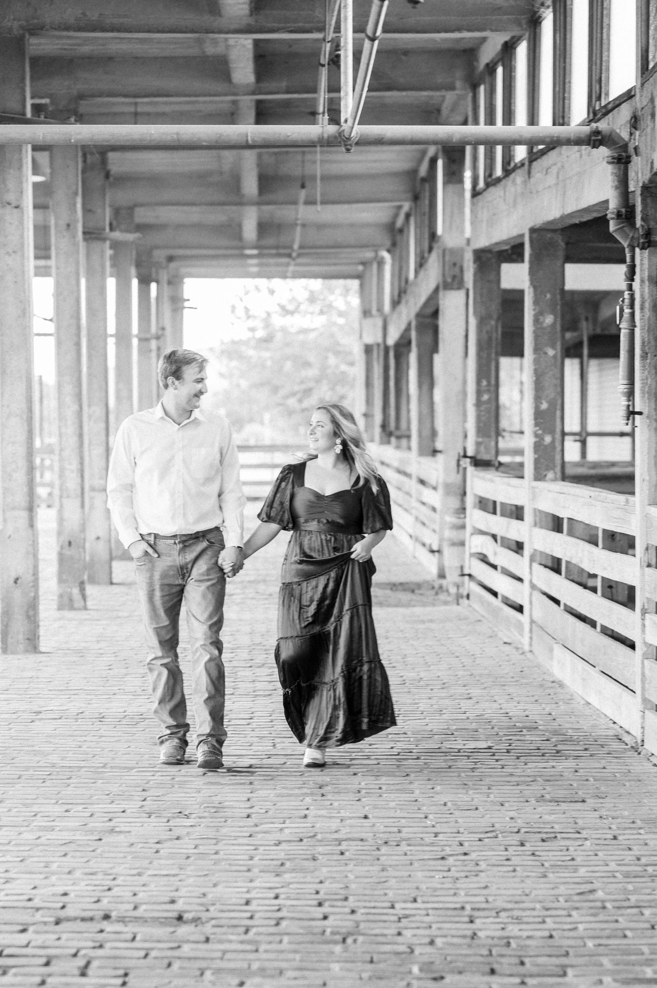 Romantic black and white engagement photos taken in a covered brick walkway with rustic architectural details.