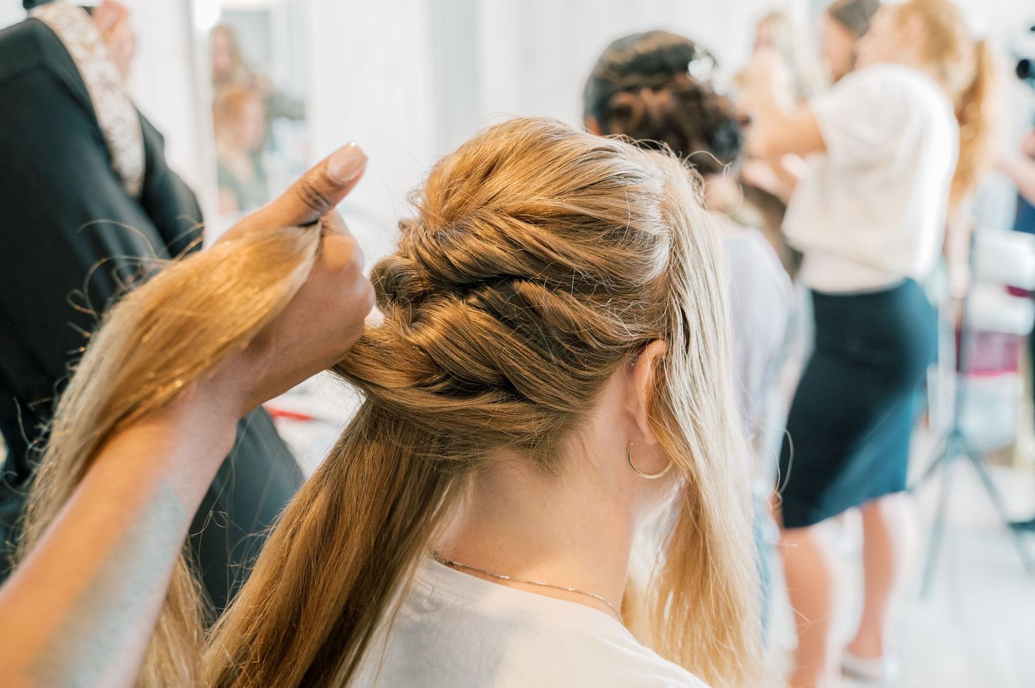 Hairstylist braiding a woman's long blonde hair in a bright salon during a styling session.