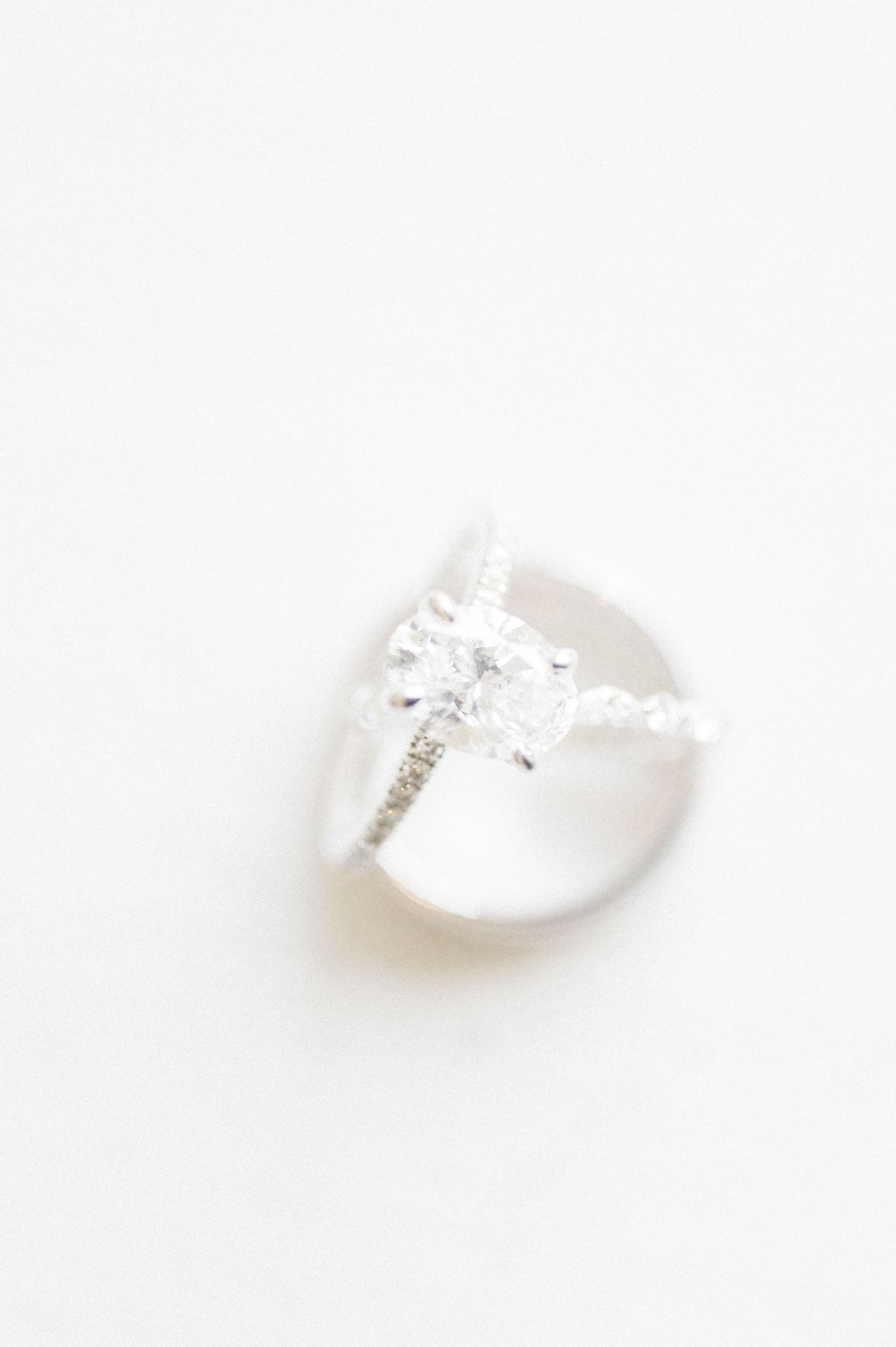 Elegant diamond solitaire engagement ring with pavé band resting on a smooth stone against white background.
