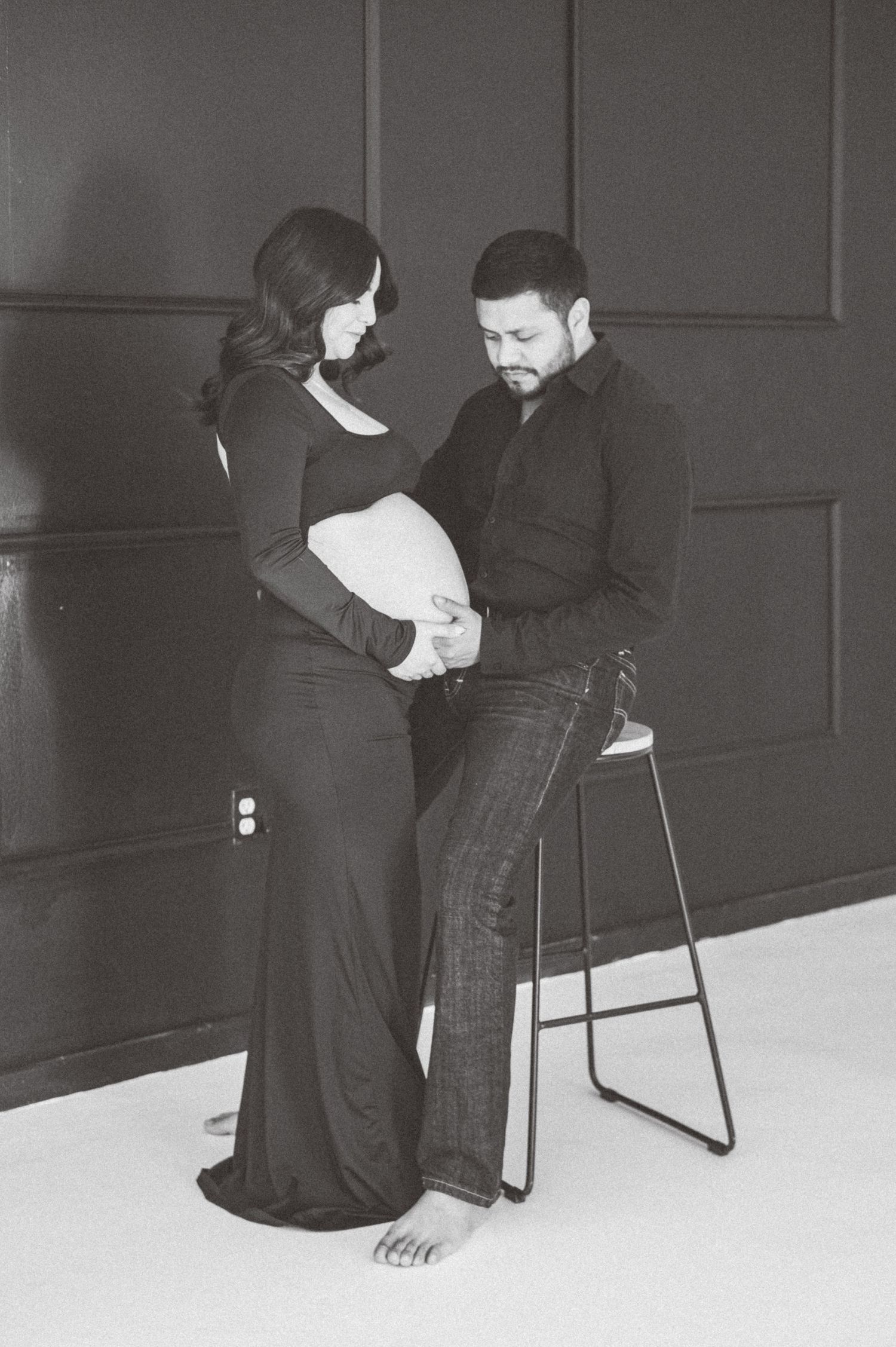 Black and white maternity photo of a couple tenderly cradling a pregnant belly in a studio setting.