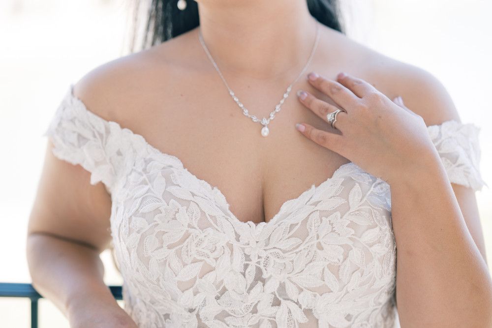 A bride in an elegant white lace wedding gown with off-shoulder details poses gracefully.