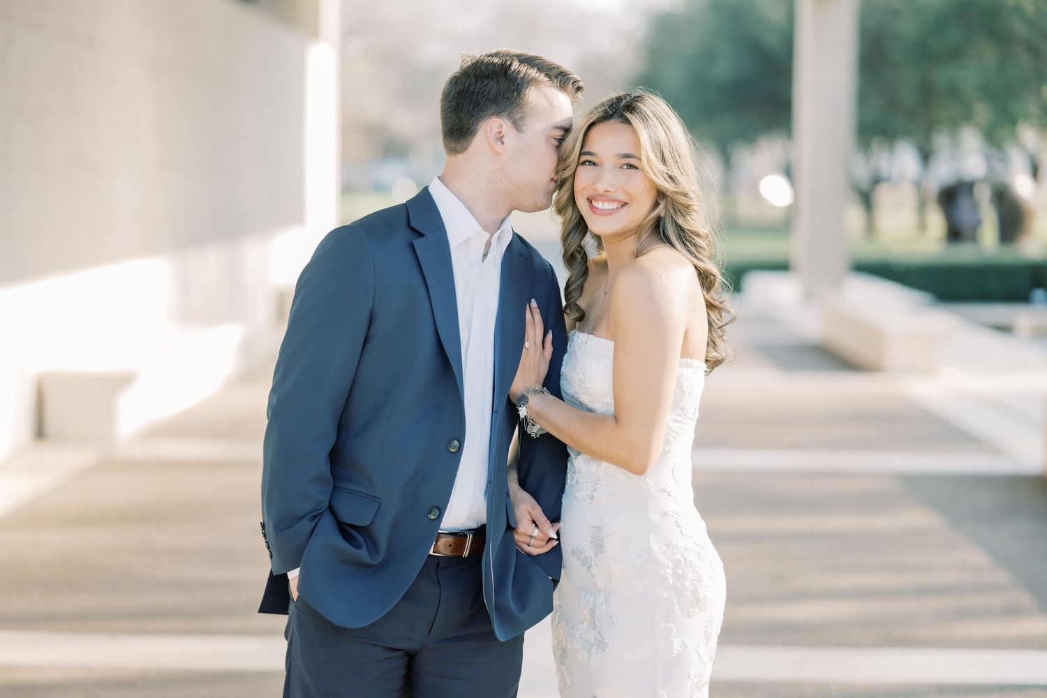 A romantic wedding couple shares intimate moments in an outdoor colonnade setting with soft natural lighting.