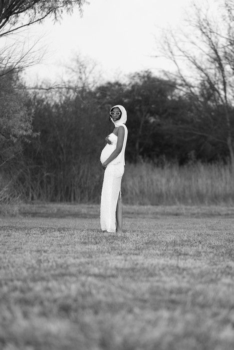 Black and white maternity photo shows a silhouette standing in a field with bare trees in the background.