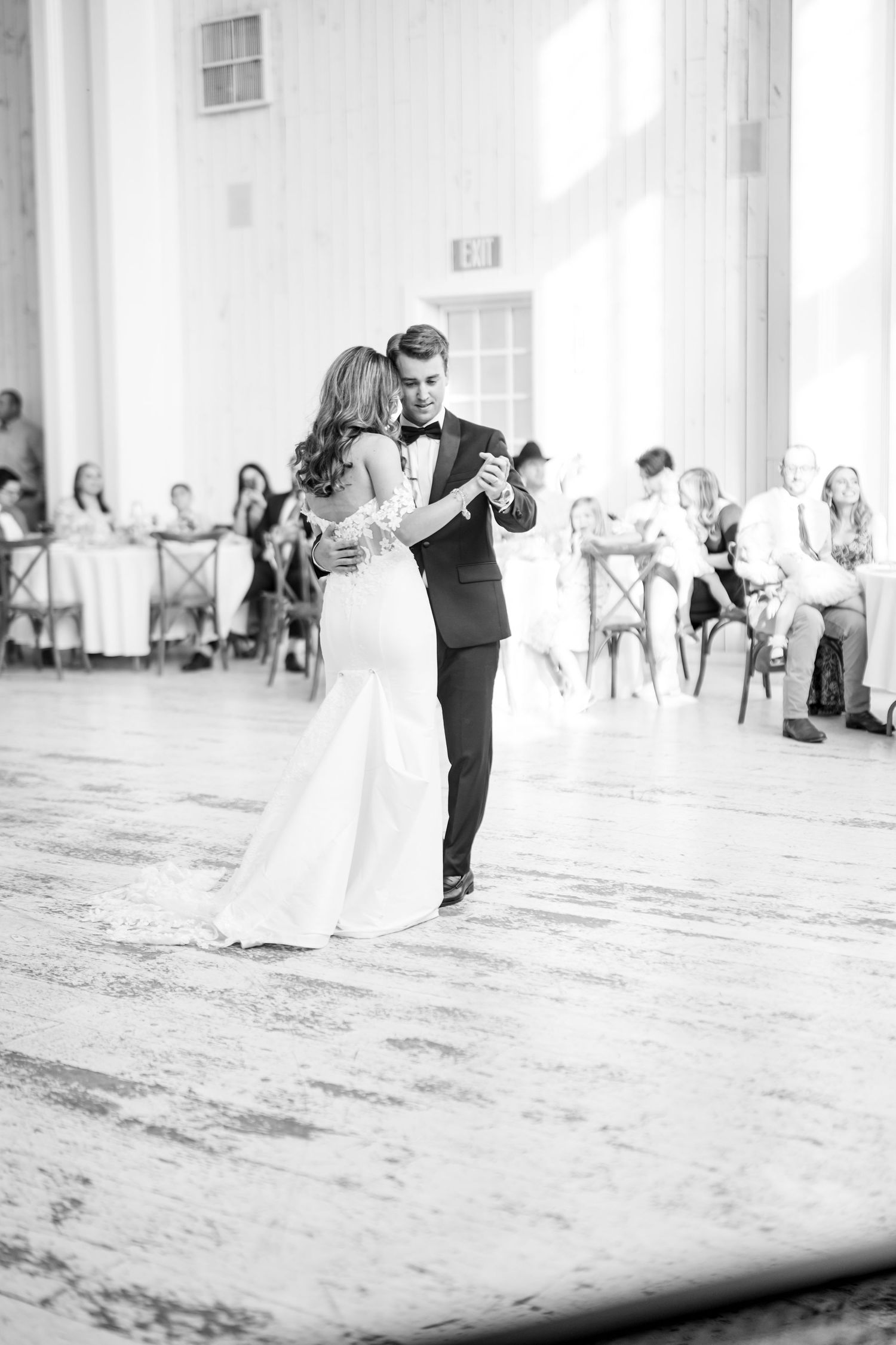 Black and white photo of bride and groom sharing romantic first dance in barn.