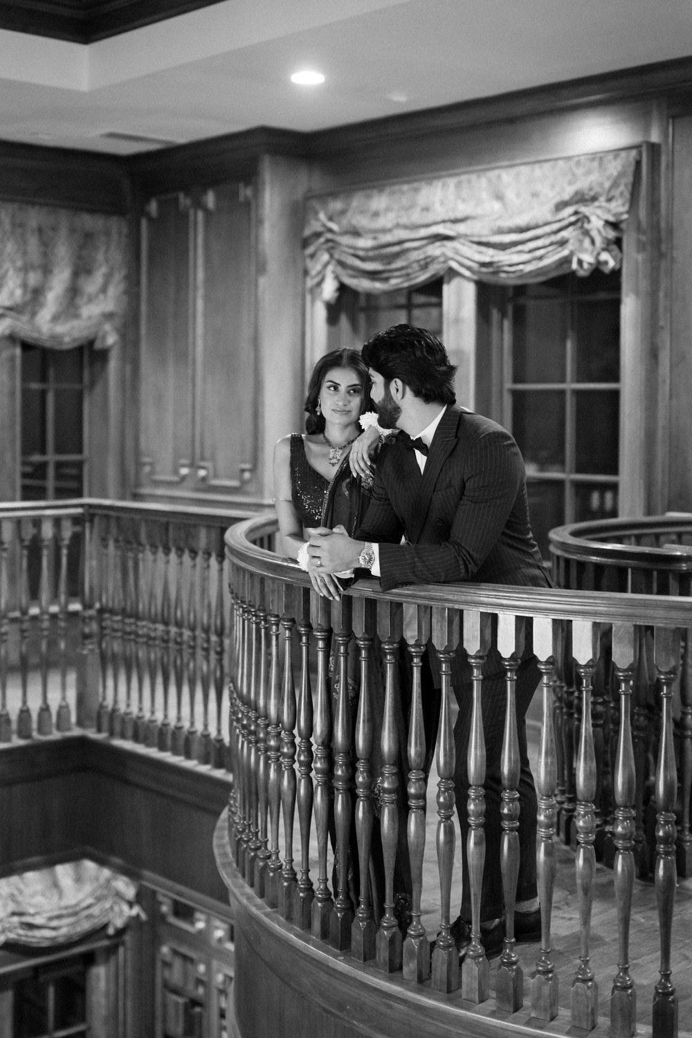 Romantic black and white photo of couple on vintage balcony with ornate railings.