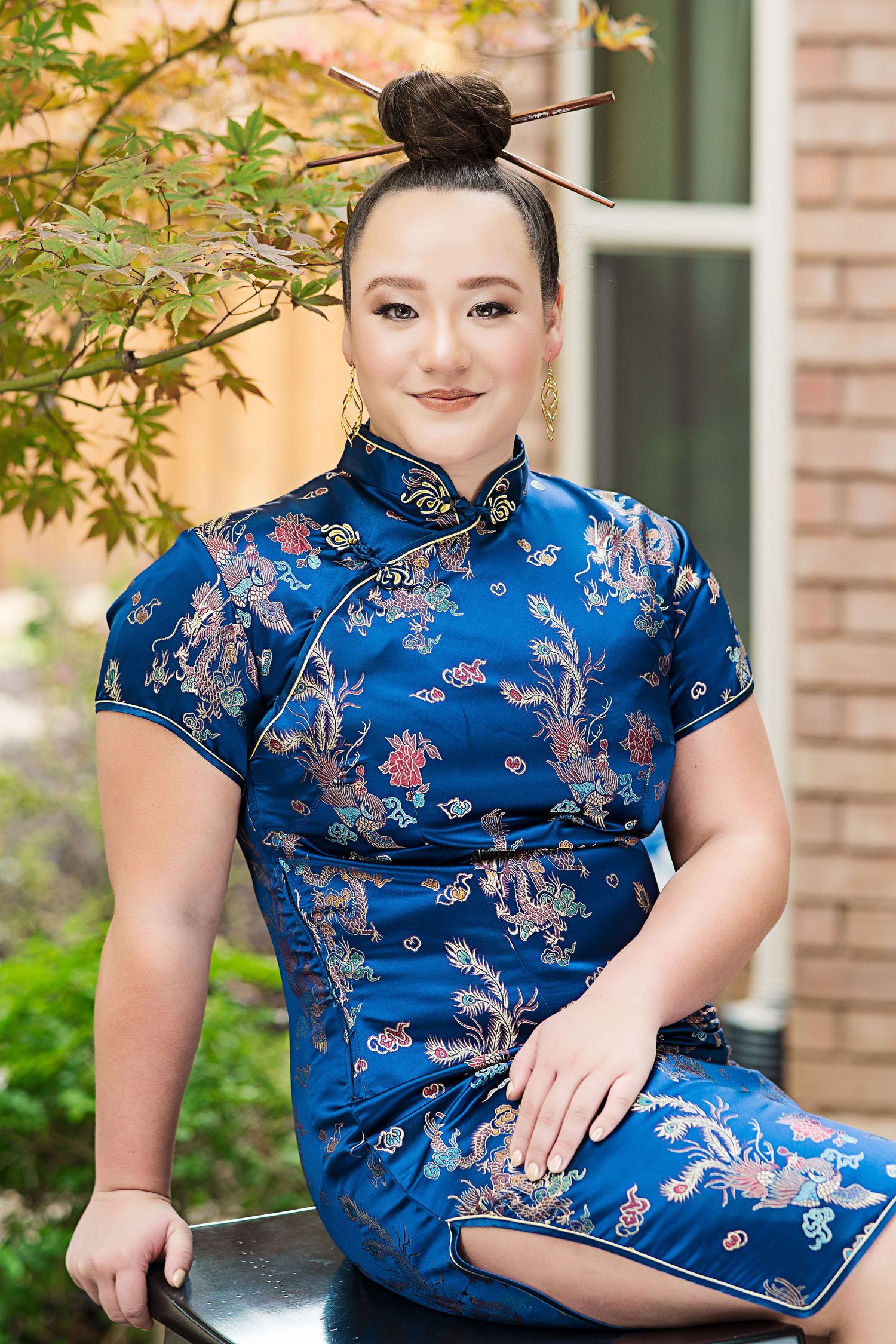 Woman wearing traditional blue Chinese qipao dress with floral pattern sitting outdoors.