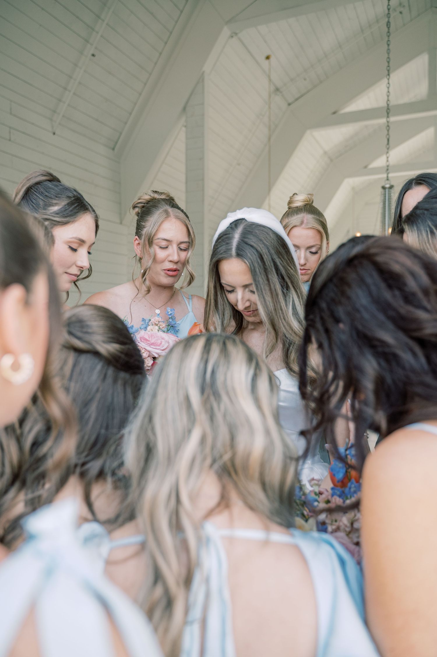 Bridesmaids in floral robes gathered in a circle with bride for pre-wedding prayer.