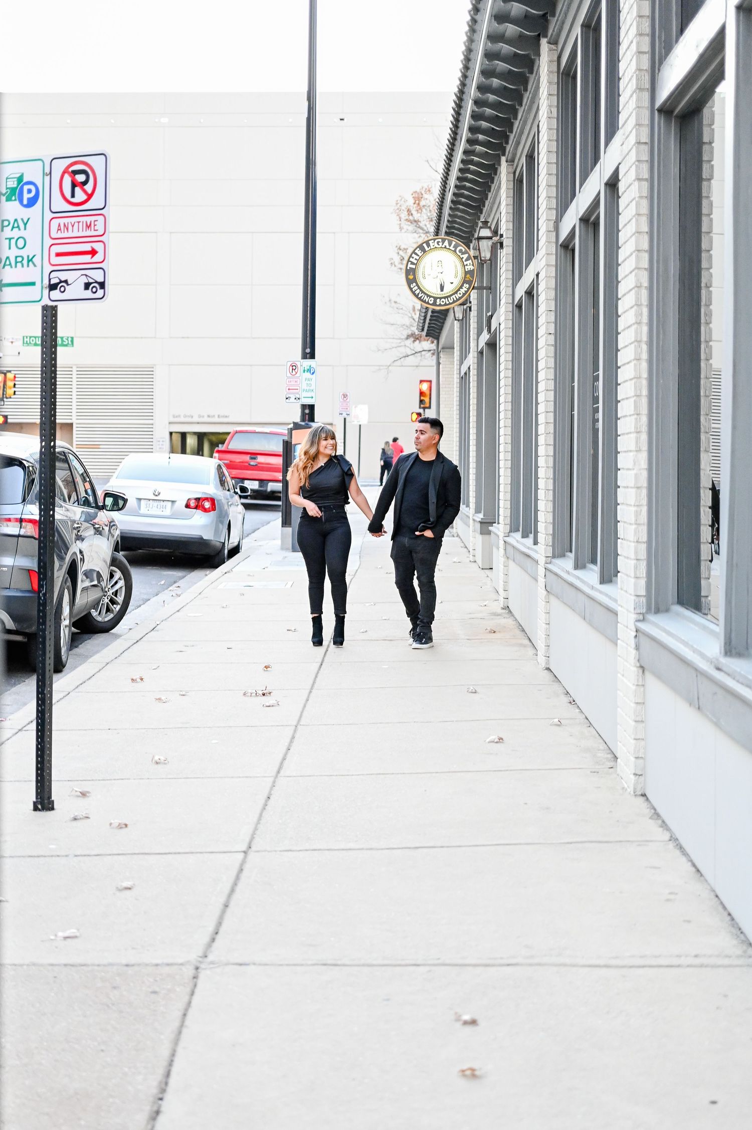 Couple dressed in black walking hand in hand along an urban city sidewalk.