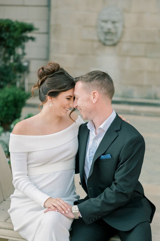 Bride and groom sharing an intimate nose-to-nose moment seated outdoors, bride in white off-shoulder gown.
