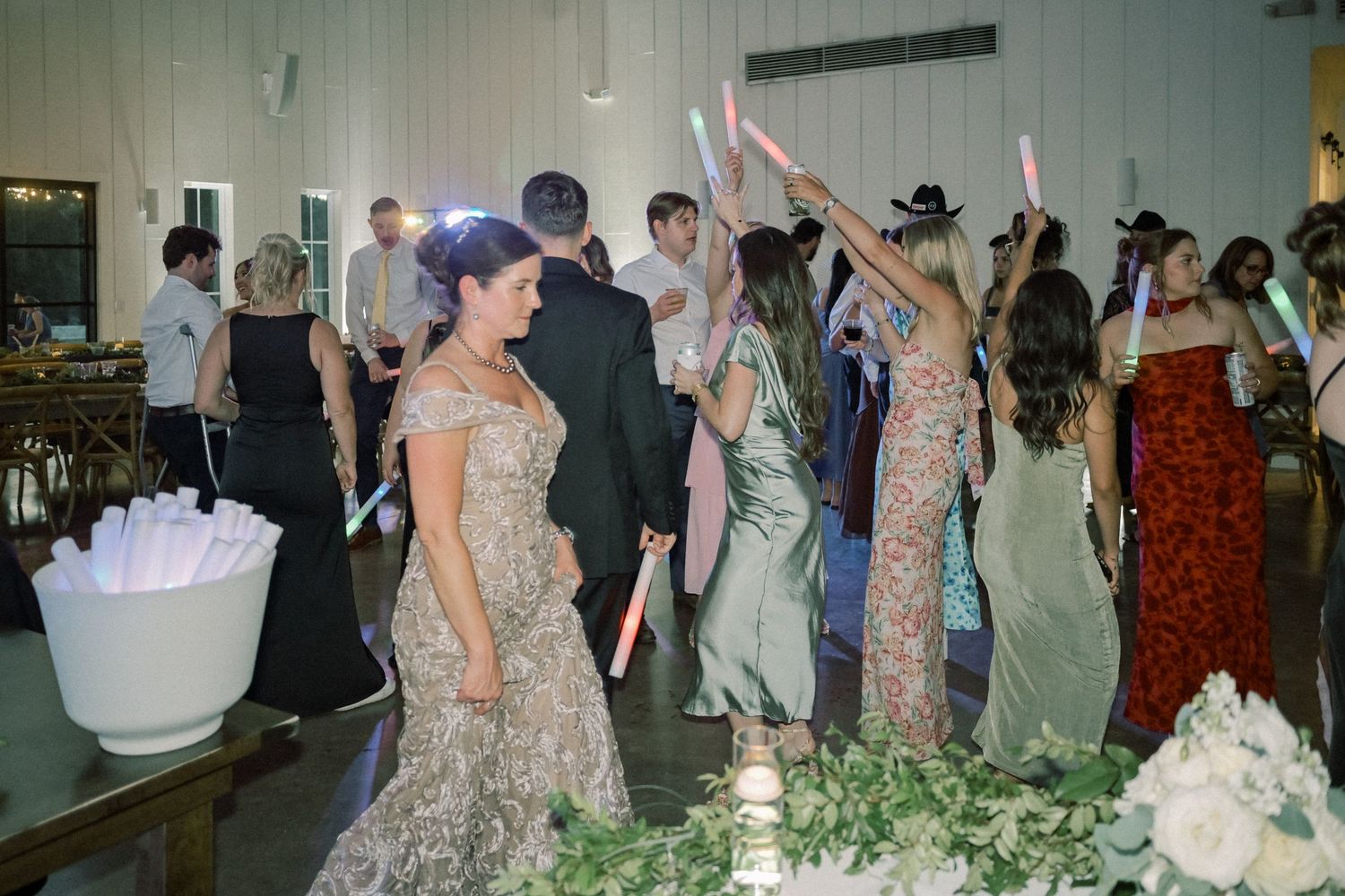 Wedding guests dance and celebrate with glowing foam sticks on the reception dance floor at night.