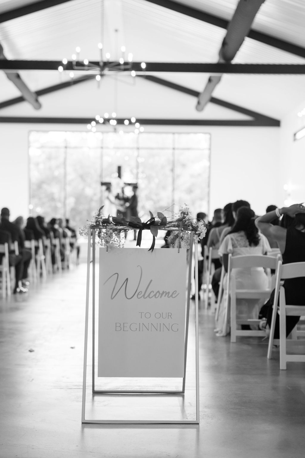 Black and white photo of a wedding ceremony venue with a Welcome to Our Beginning sign at the aisle entrance.