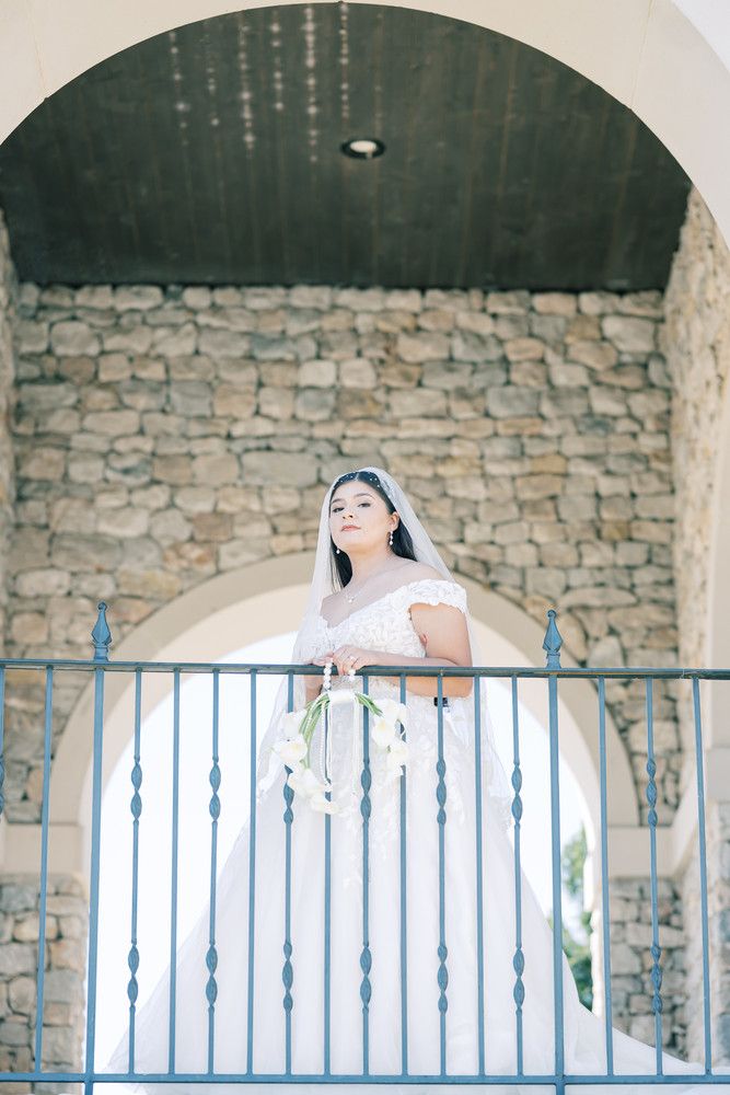 Bride in a white dress poses along a stone wall with decorative blue metal railings.