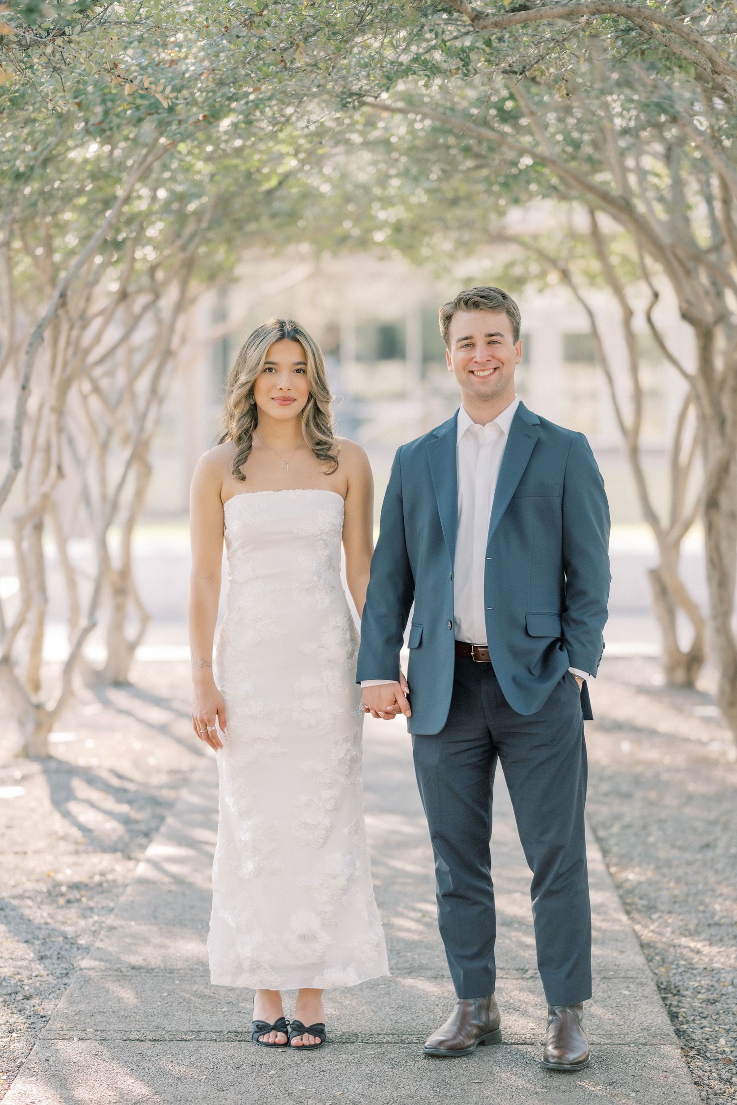 A couple in wedding attire poses together in a wooded outdoor setting with soft natural lighting.