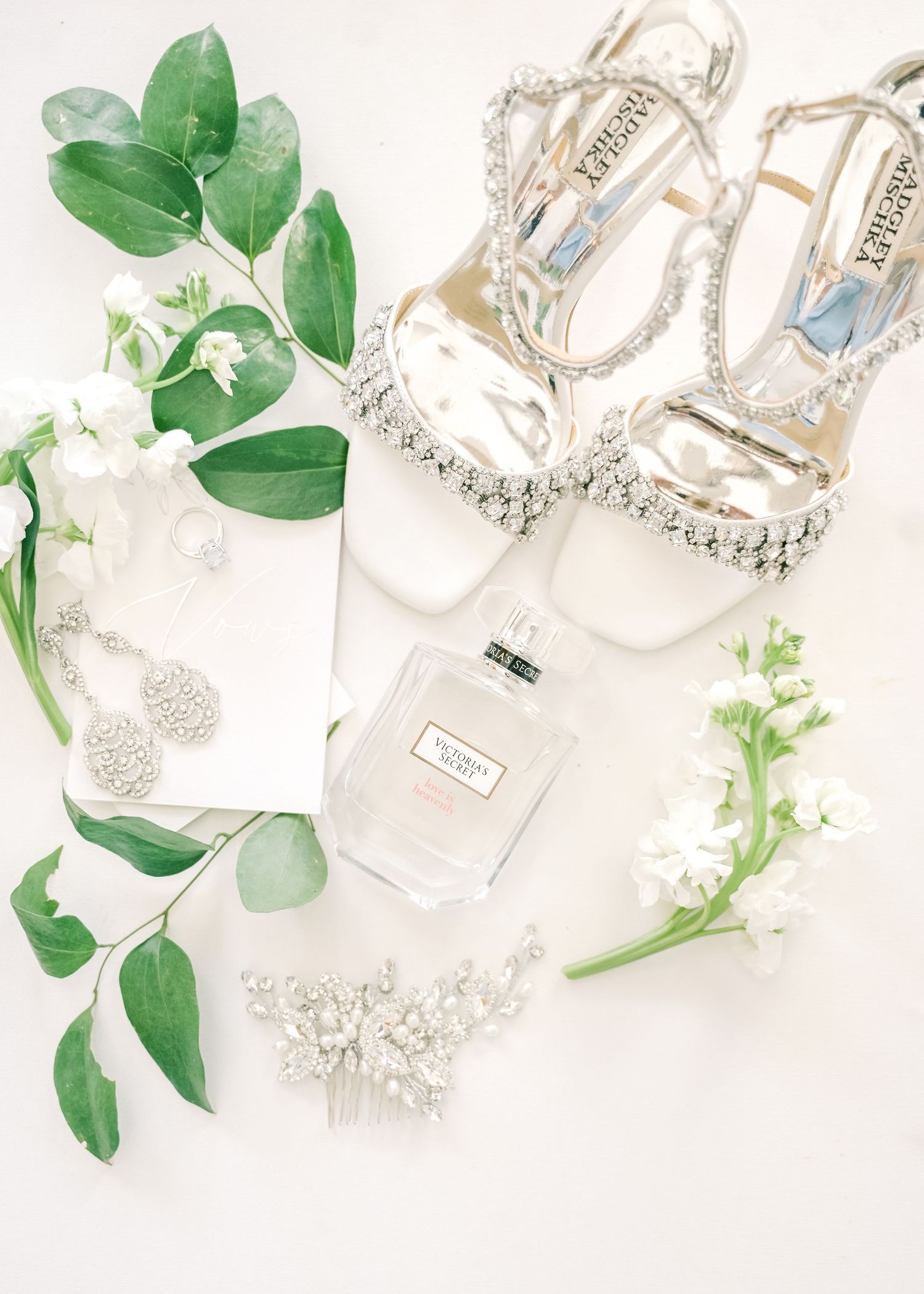 Wedding accessories including crystal headpieces and green foliage arranged on white background.