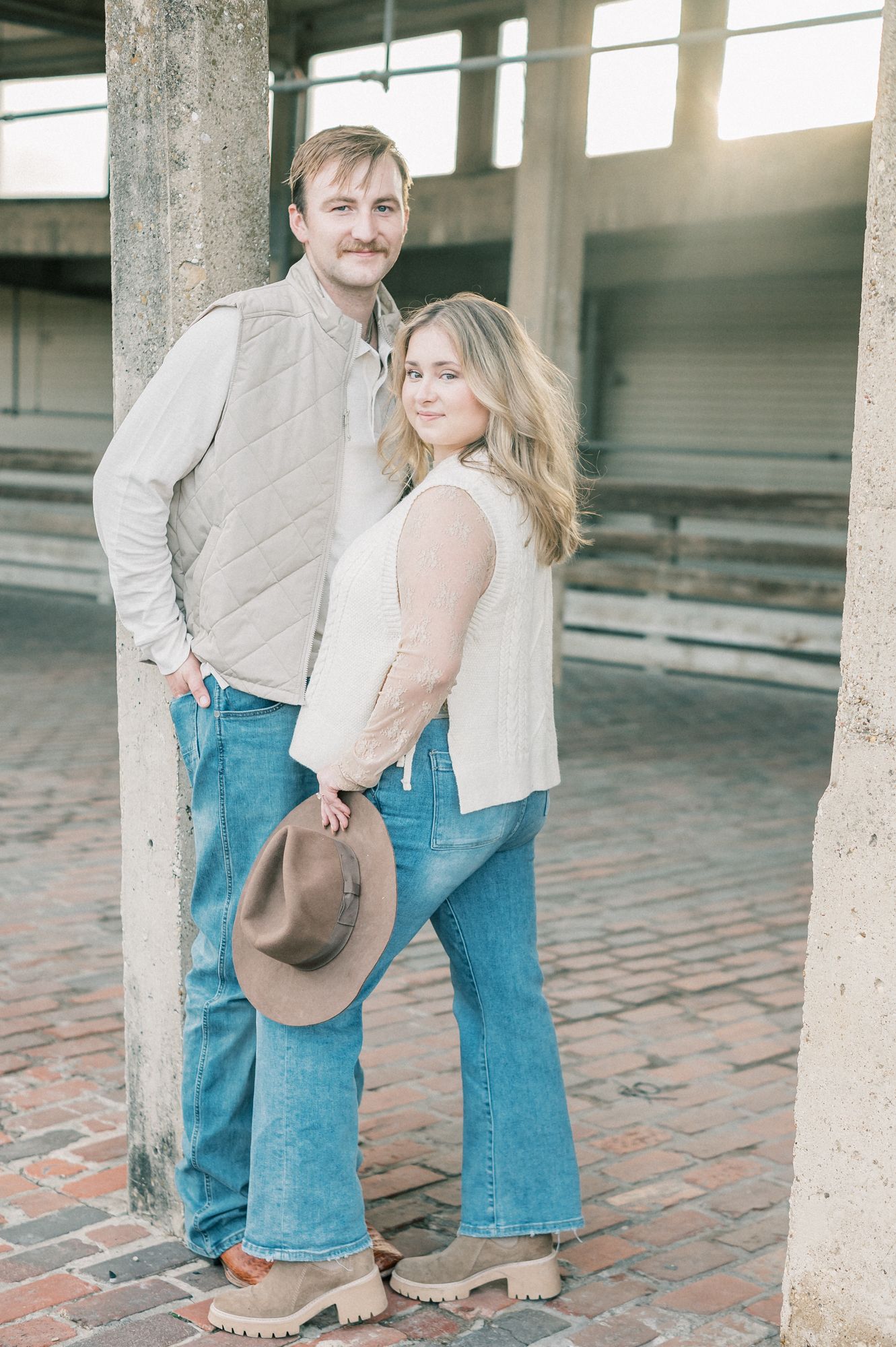 A couple in matching casual attire poses together in front of an industrial-style building with natural lighting.