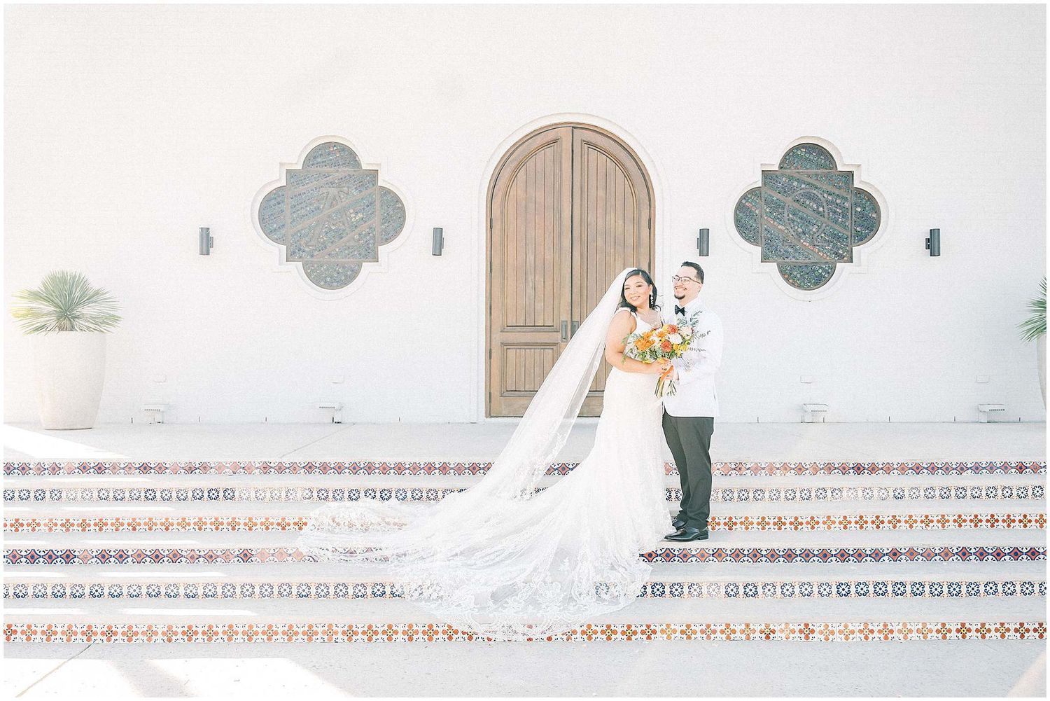 Wedding couple posing against white Spanish mission-style architecture with decorative details.
