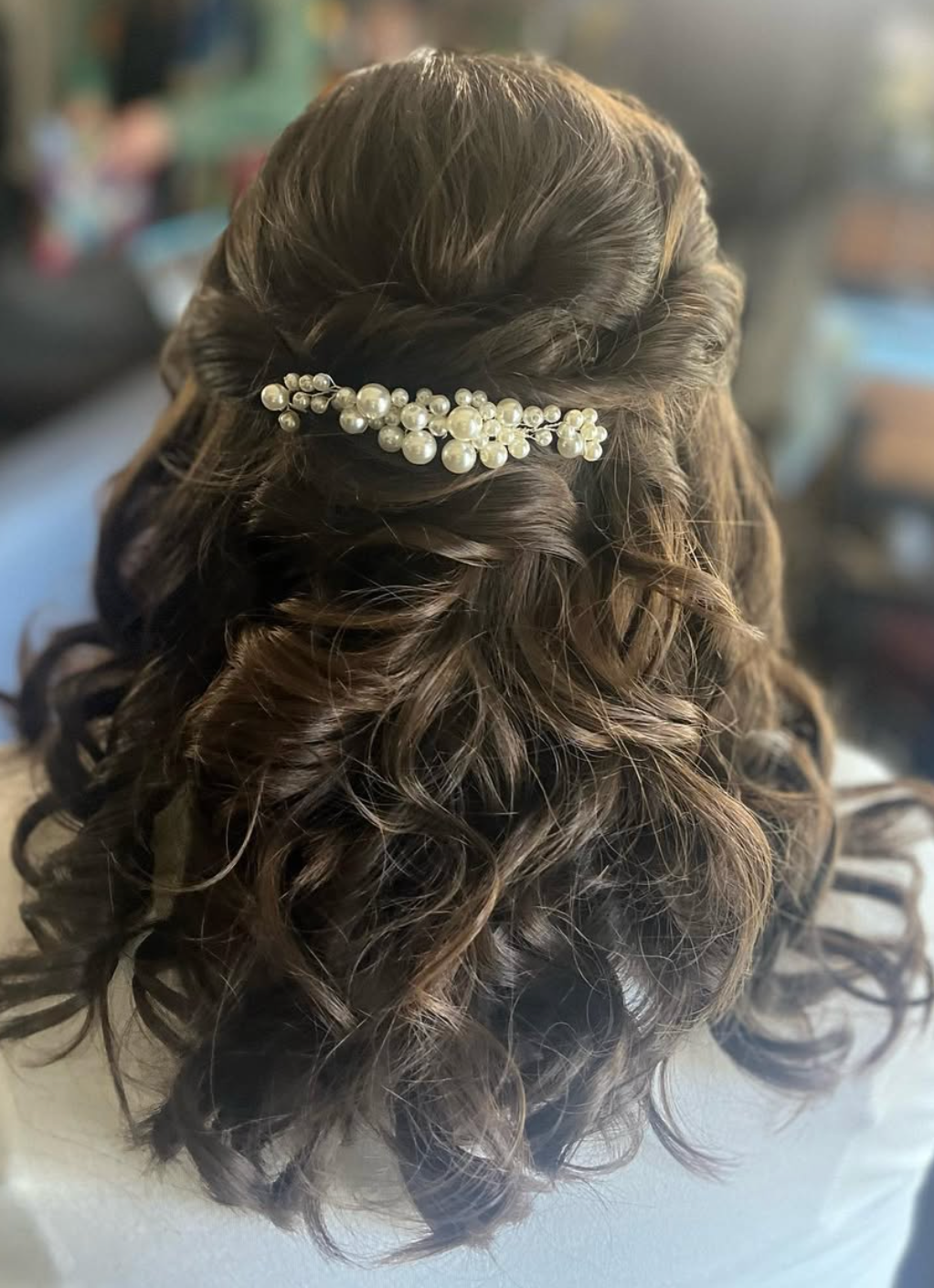 Elegant half-up hairstyle with loose curls adorned with a pearl floral hair comb for a bridal look.