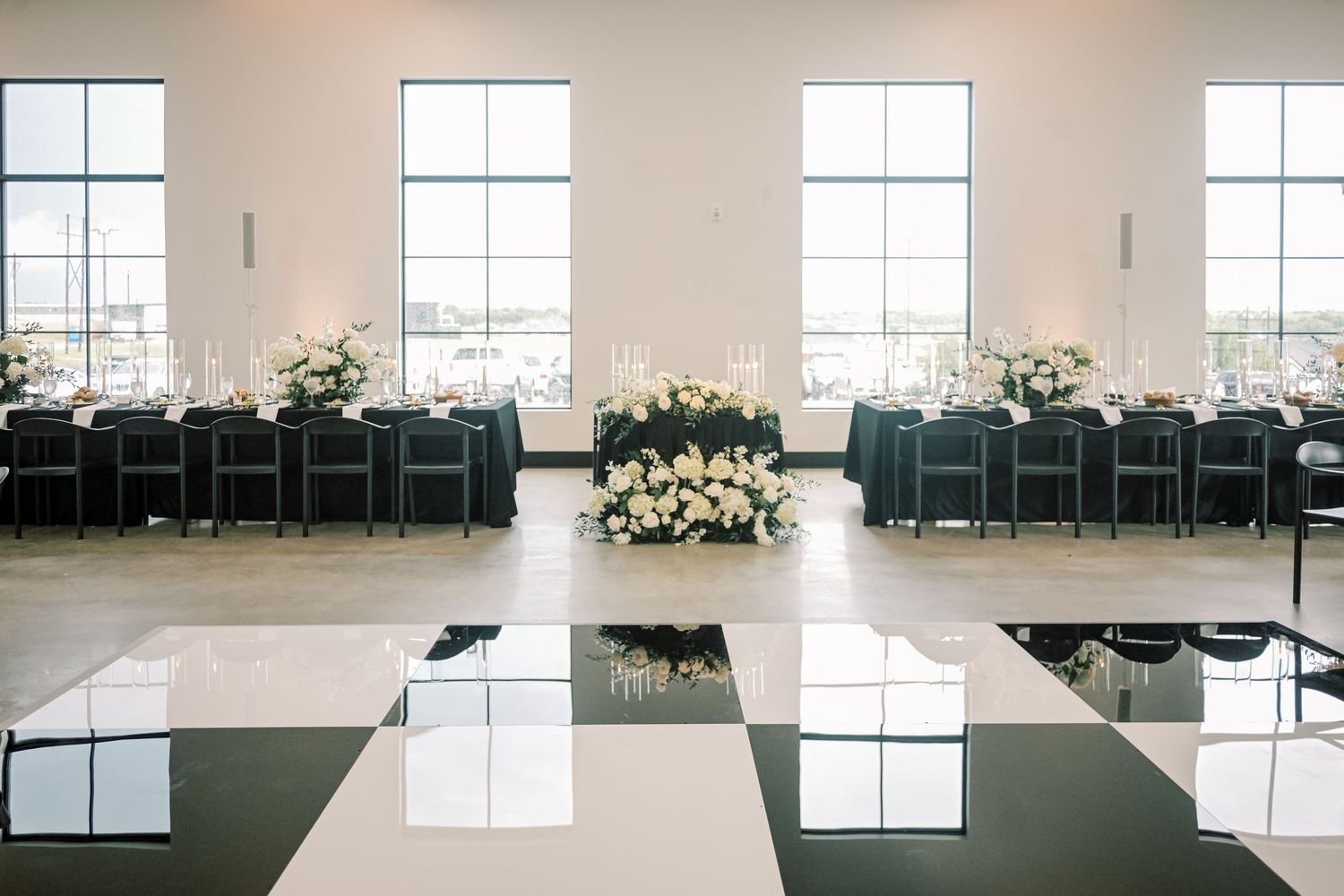 Elegant black and white wedding reception hall with checkered dance floor, floral centerpieces, and long dining tables.
