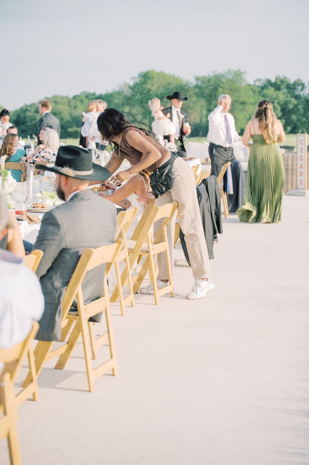 Outdoor wedding ceremony setup with wooden chairs and guests in sage green attire.