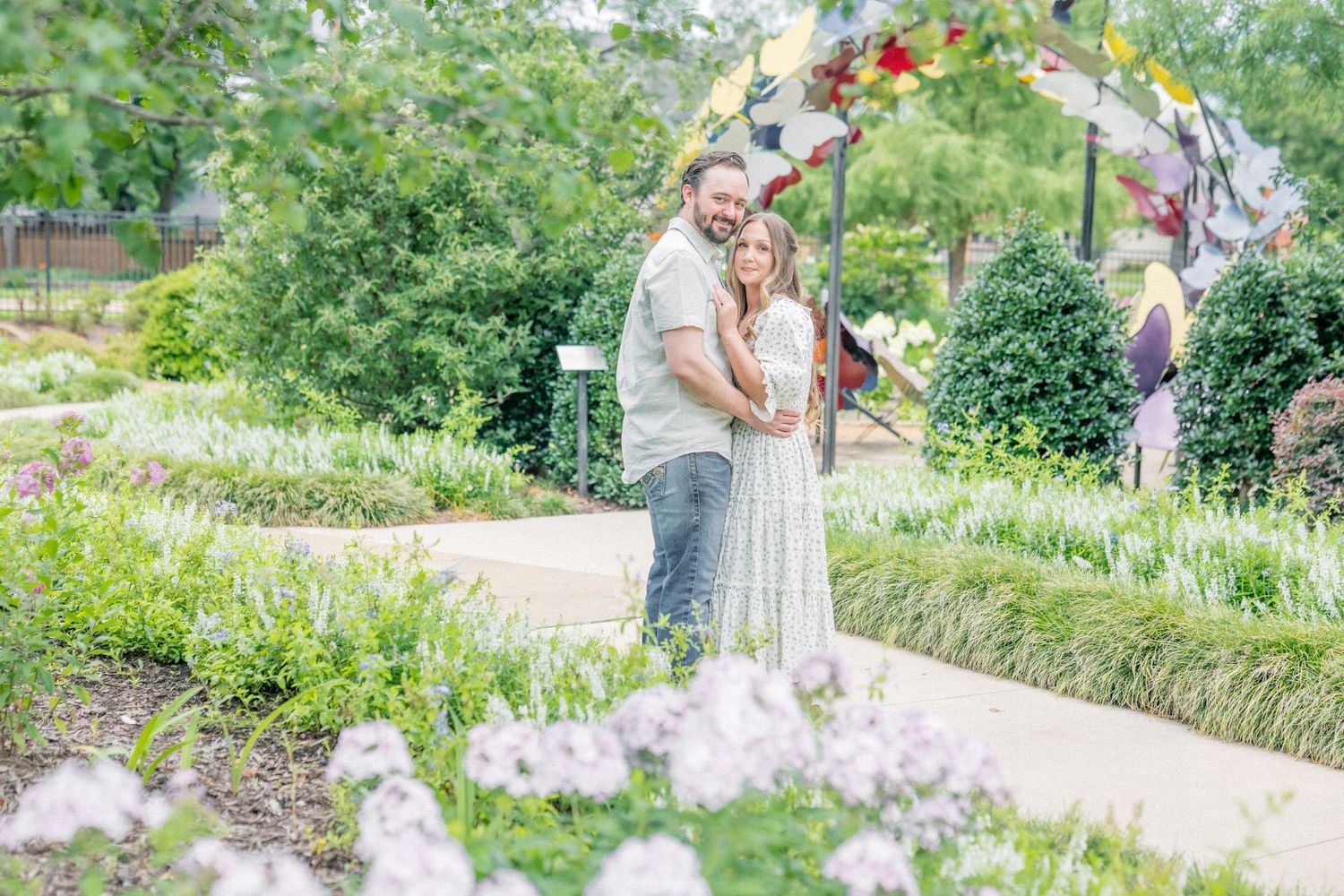 Couple embracing in a lush garden with colorful flowers and decorative pinwheels on a sunny day.