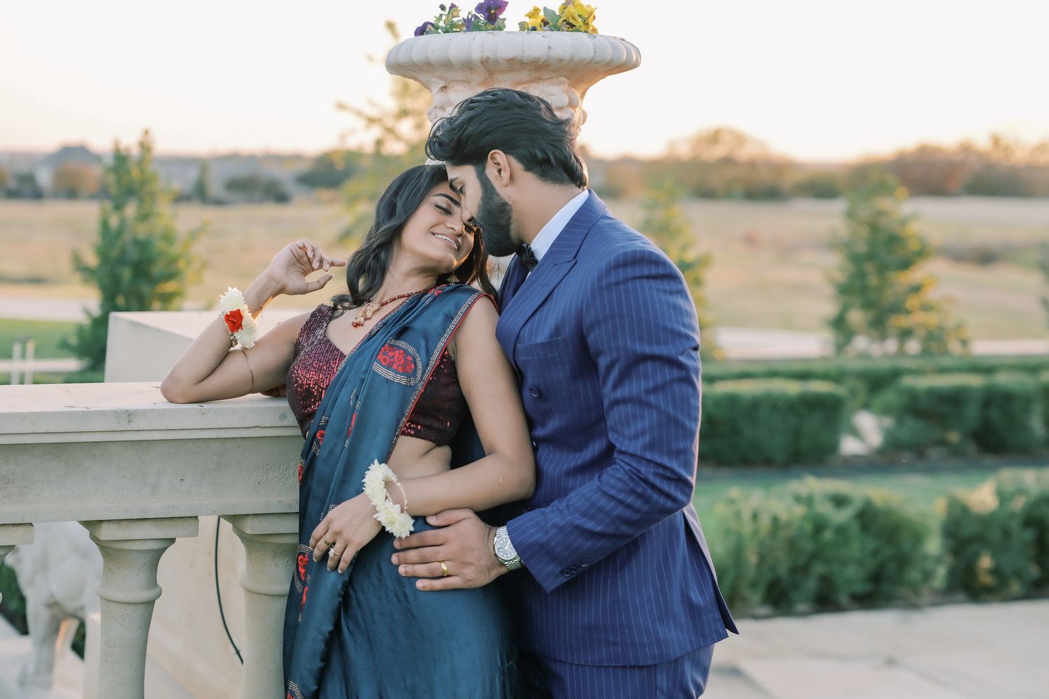 Romantic couple embraces on an outdoor balcony at sunset wearing formal attire.