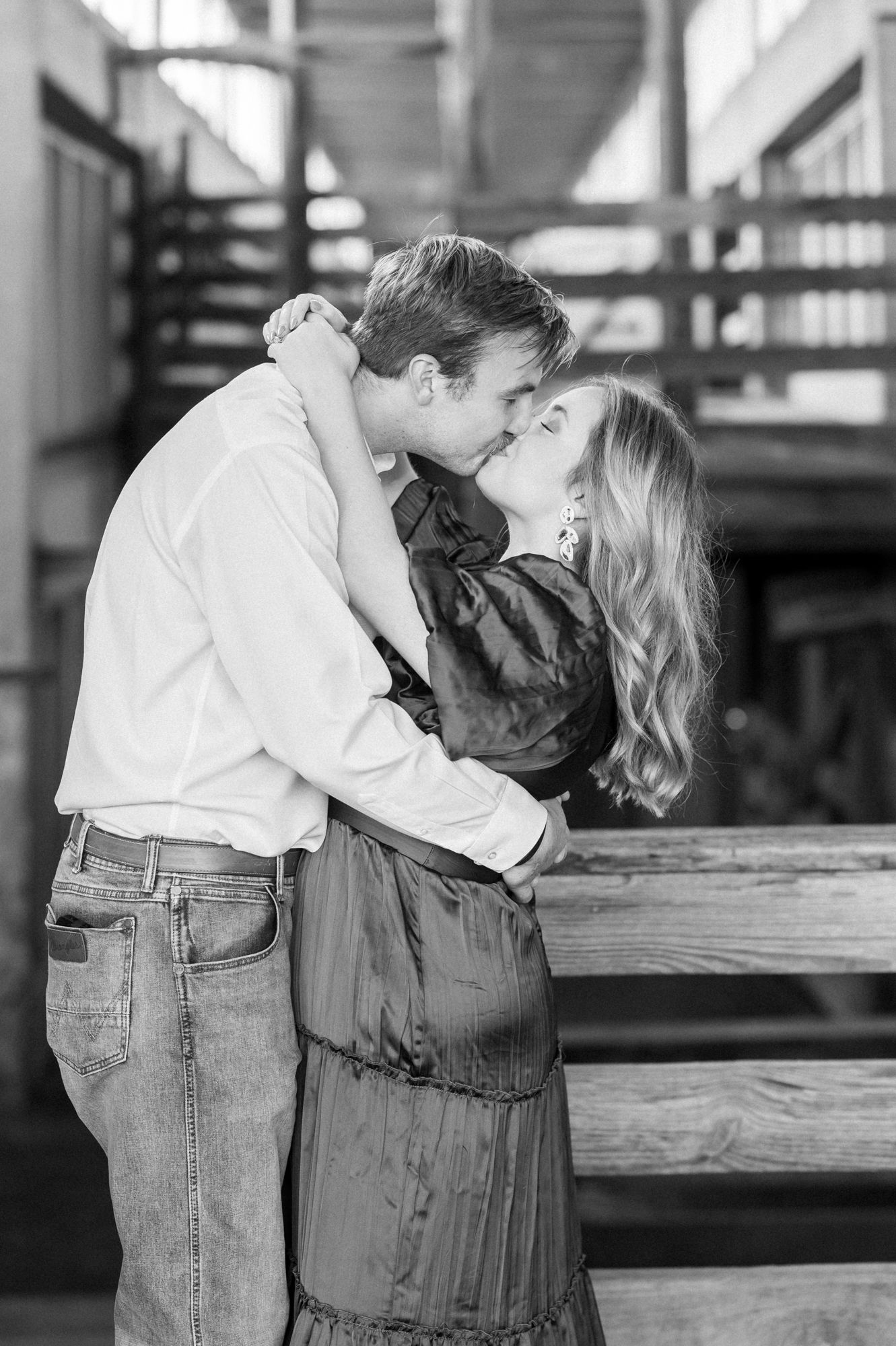 Black and white photo of couple sharing romantic moments by rustic wooden railings.