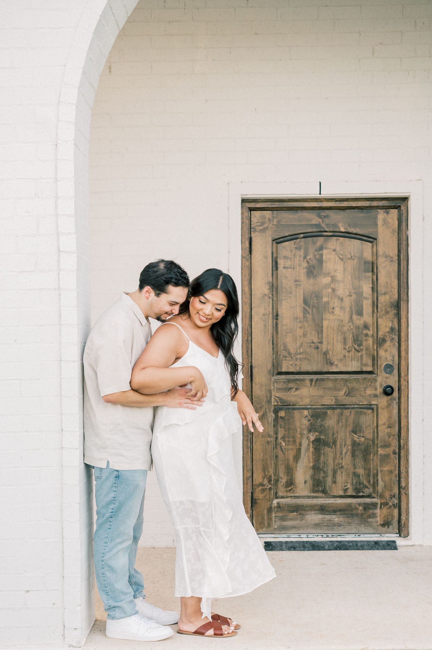 A couple shares an intimate moment in a white archway with rustic wooden doors.