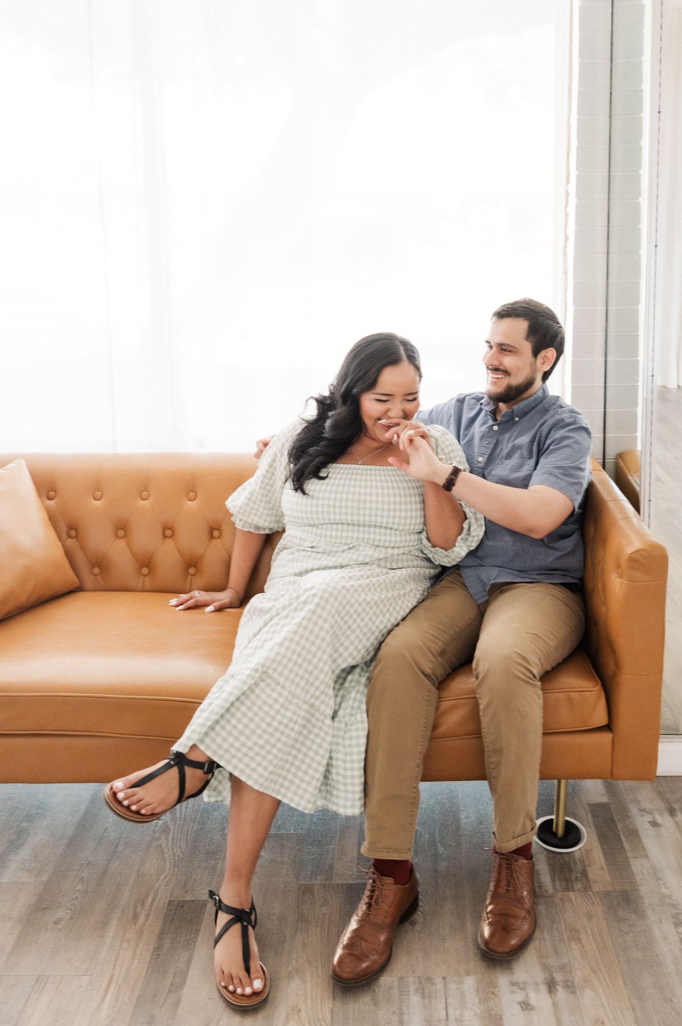 A couple sharing a playful moment on a camel-colored tufted sofa in a bright room.