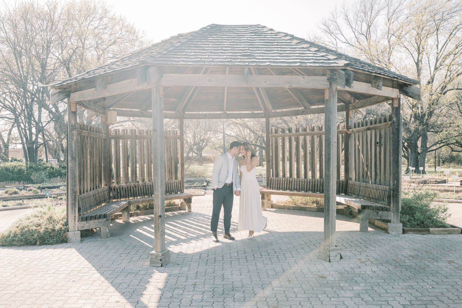A panoramic view of a rustic wooden pavilion structure in a park during winter with bare trees in the background.