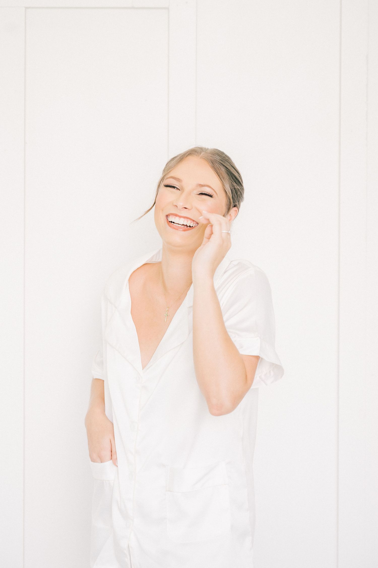 A person in a white robe laughs joyfully against a bright white background during wedding preparations.