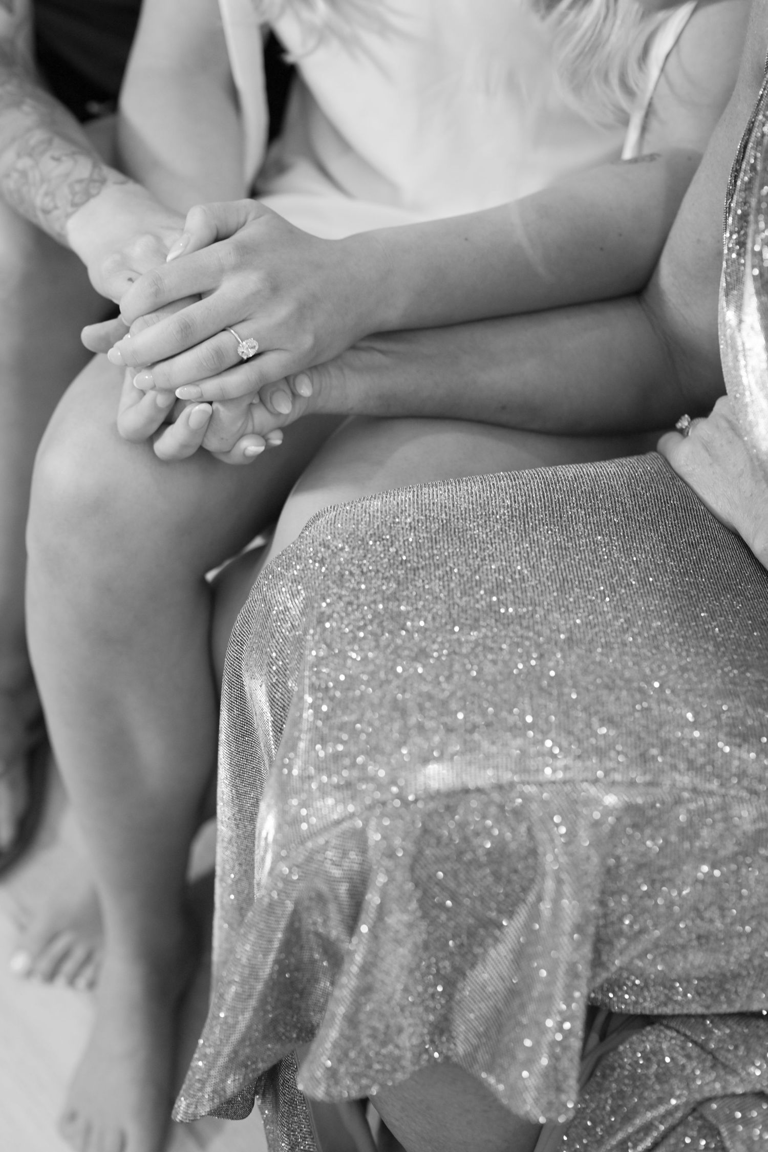 Close-up black and white photo of bride and groom holding hands, showcasing wedding ring during ceremony.