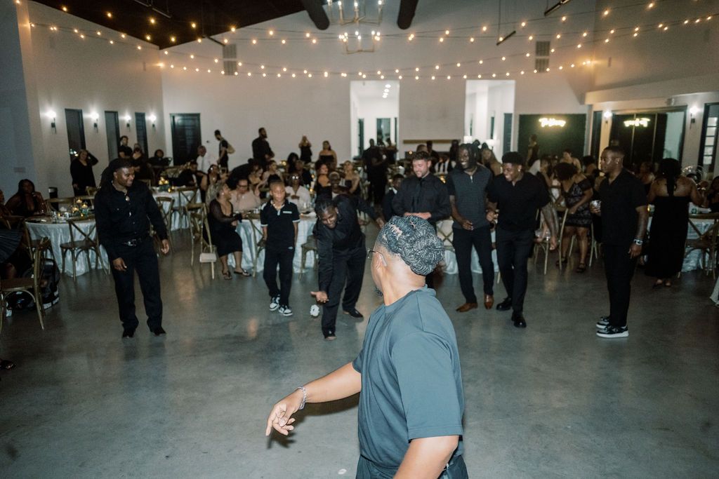 Guests gather in an elegant event hall with string lights and white chairs during a lively indoor celebration.