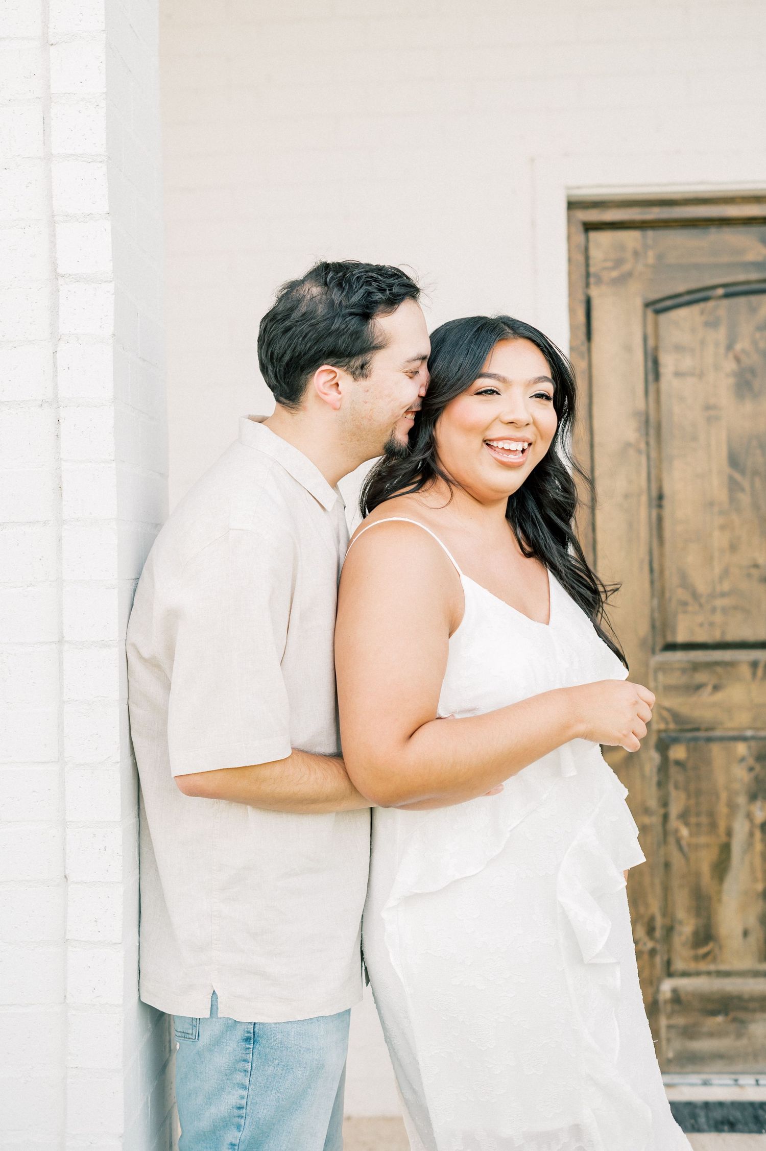 A couple in white outfits share tender moments together against a rustic wooden door background.