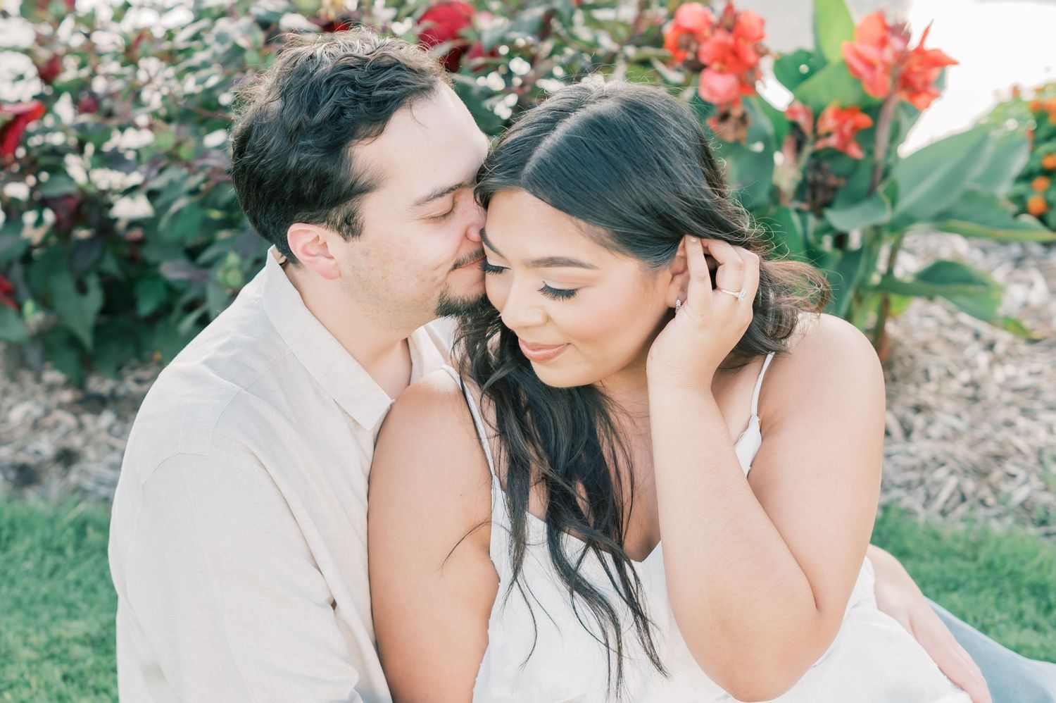 Romantic outdoor photo shoot in a garden with red flowers and greenery in the background.