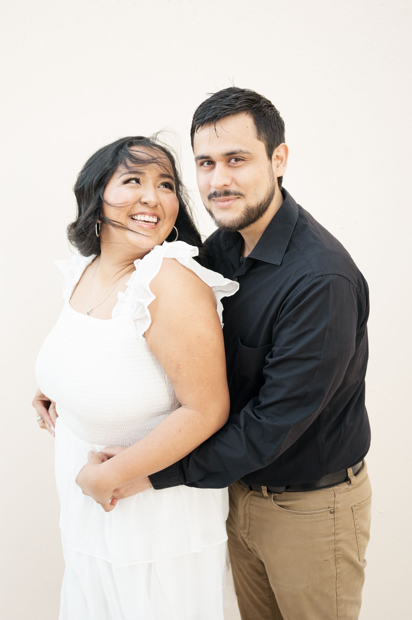 A couple embraces while wearing coordinated white and black outfits in a minimalist setting.